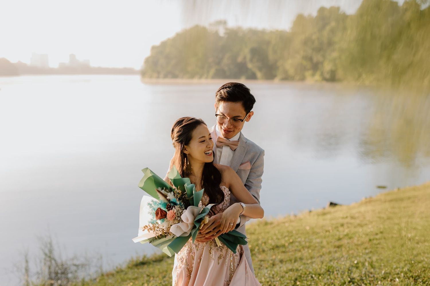 Sunlit engagement photos captured beside tranquil lake with gentle embraces.