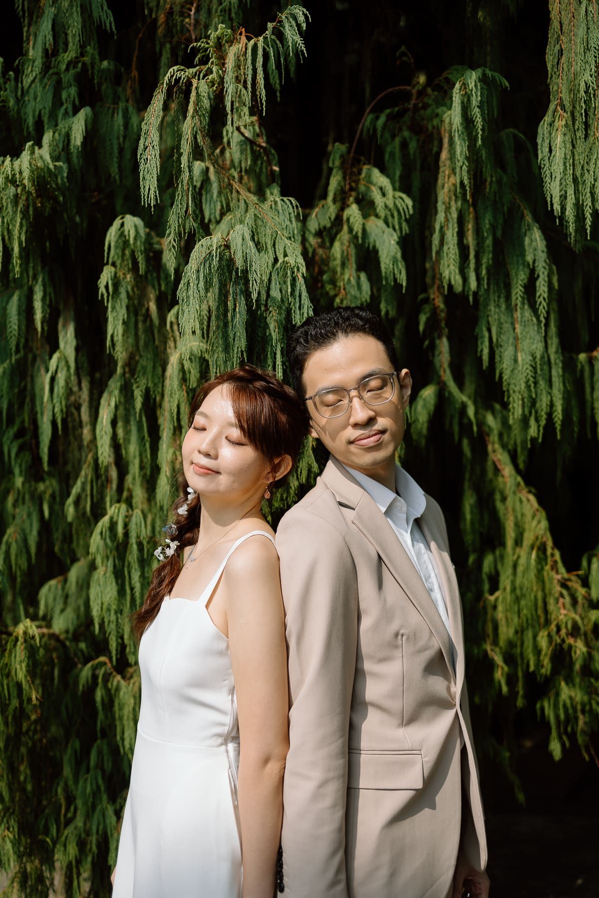 A stylish wedding portrait against a backdrop of cascading willow branches in natural sunlight.