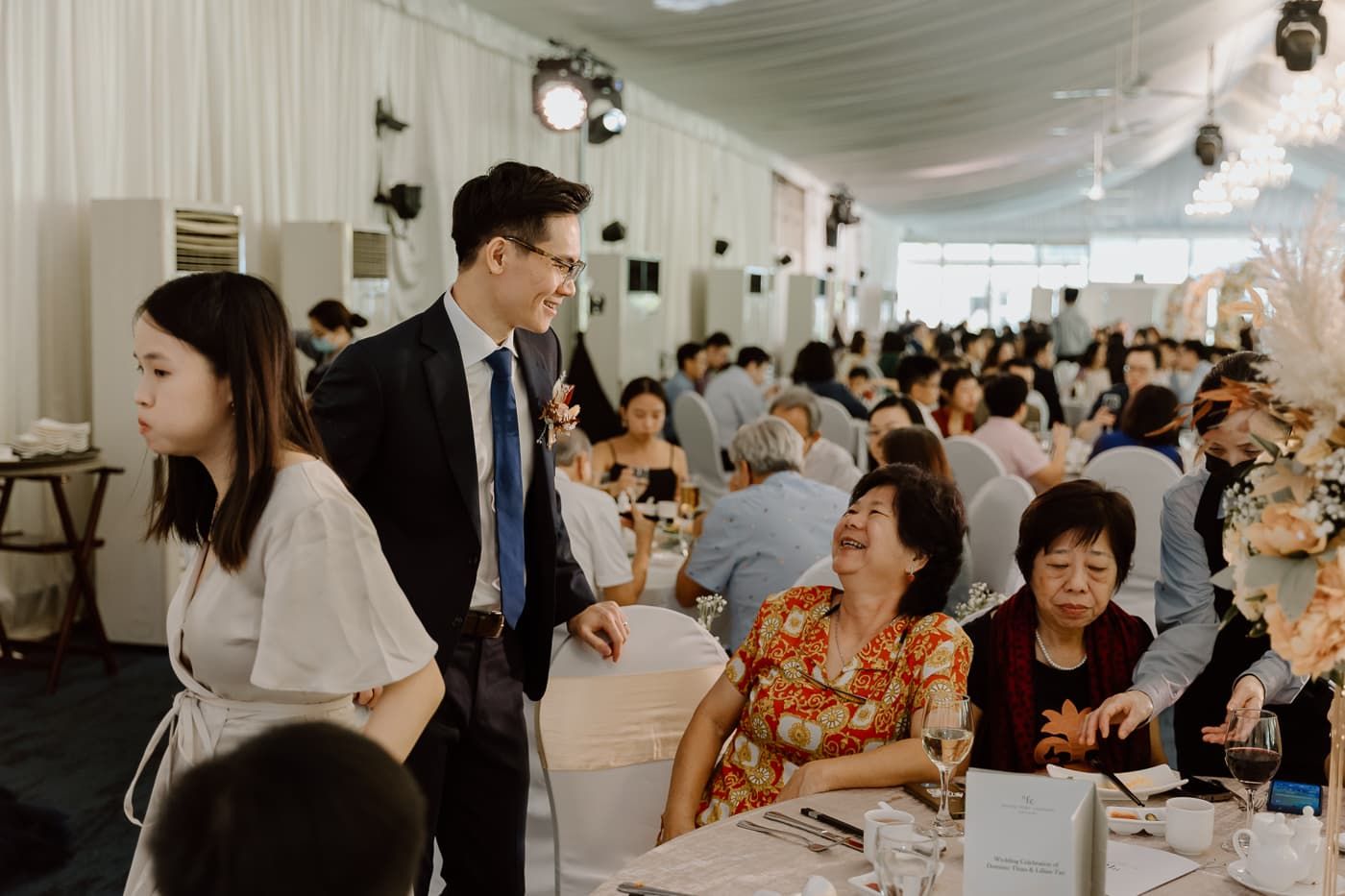 Guests interact during a wedding reception in a white draped venue.