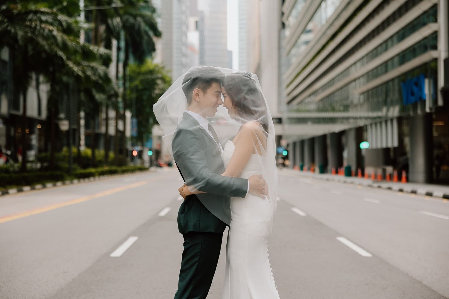 A romantic wedding couple shares an intimate moment under a veil on a city street.