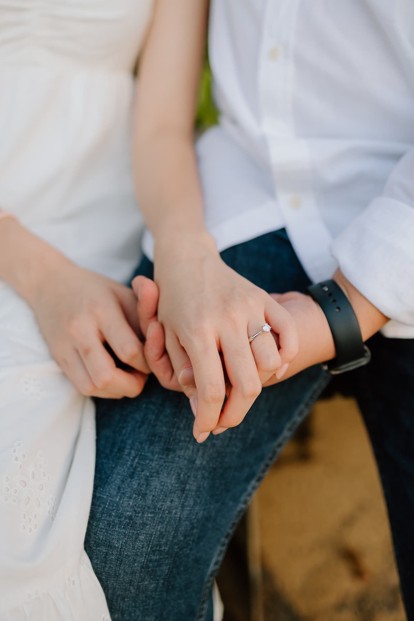 Close-up of hands with engagement ring resting on denim jeans.