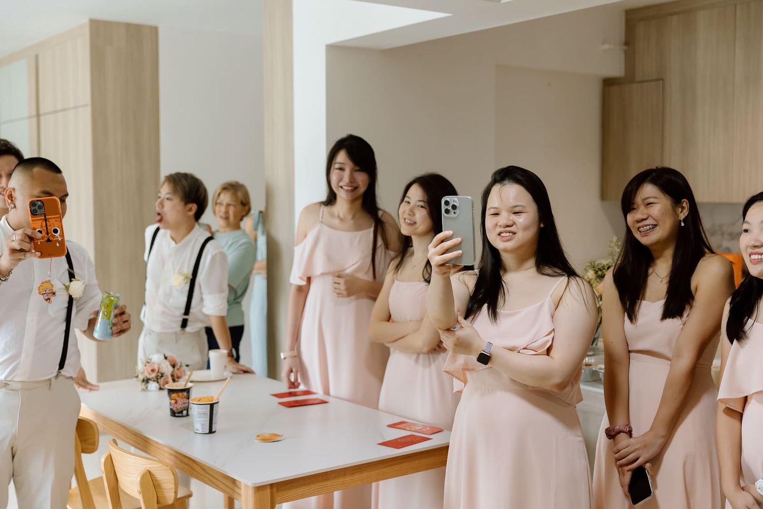 Wedding party members in pink dresses and suits gather around a table with refreshments.
