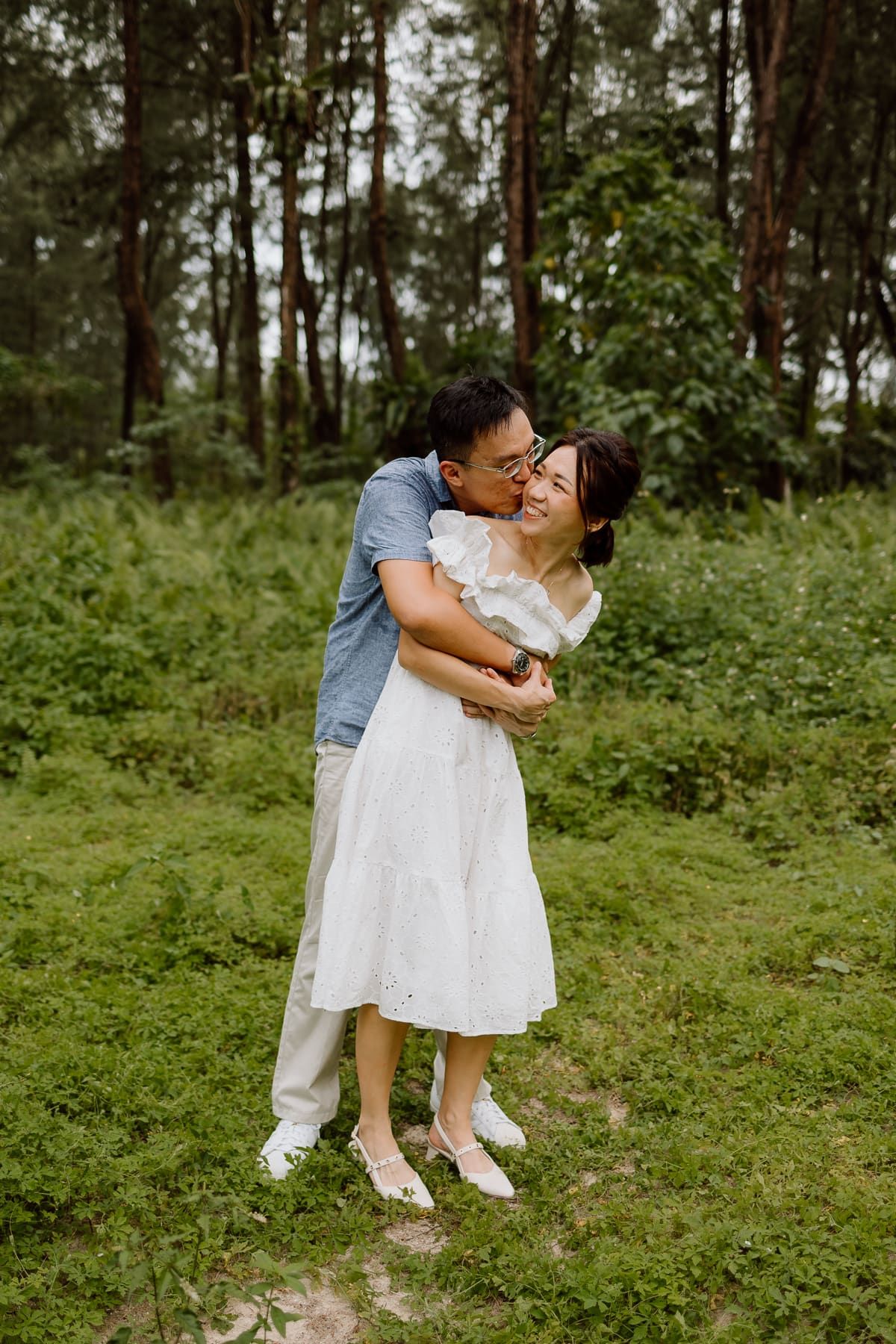 A romantic embrace between a couple wearing blue and white outfits in a lush forest setting.