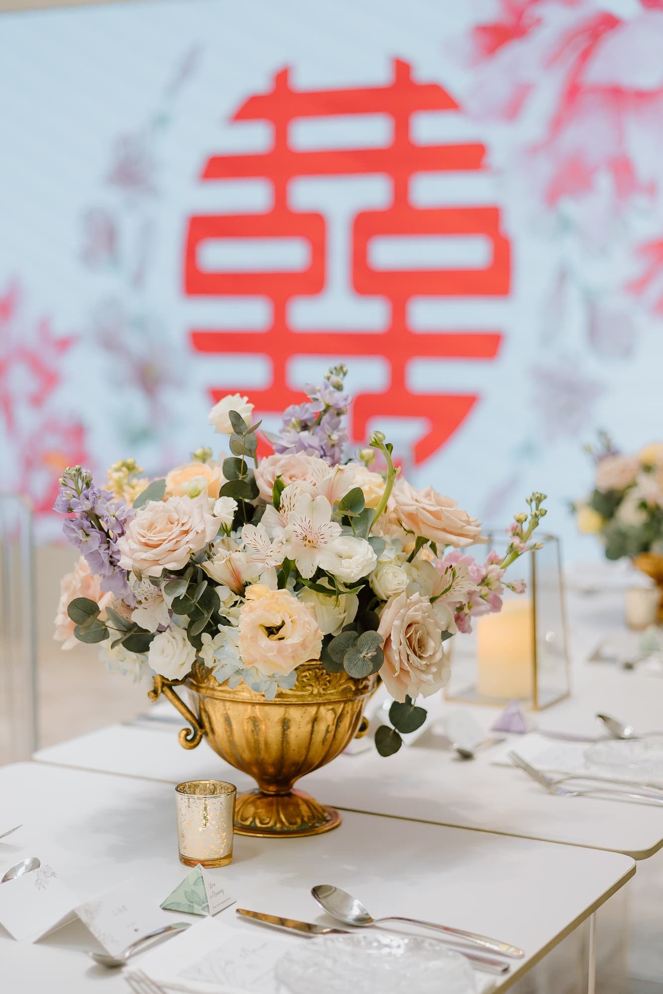 Wedding reception table decorated with blush roses in gold vases and double happiness symbol.