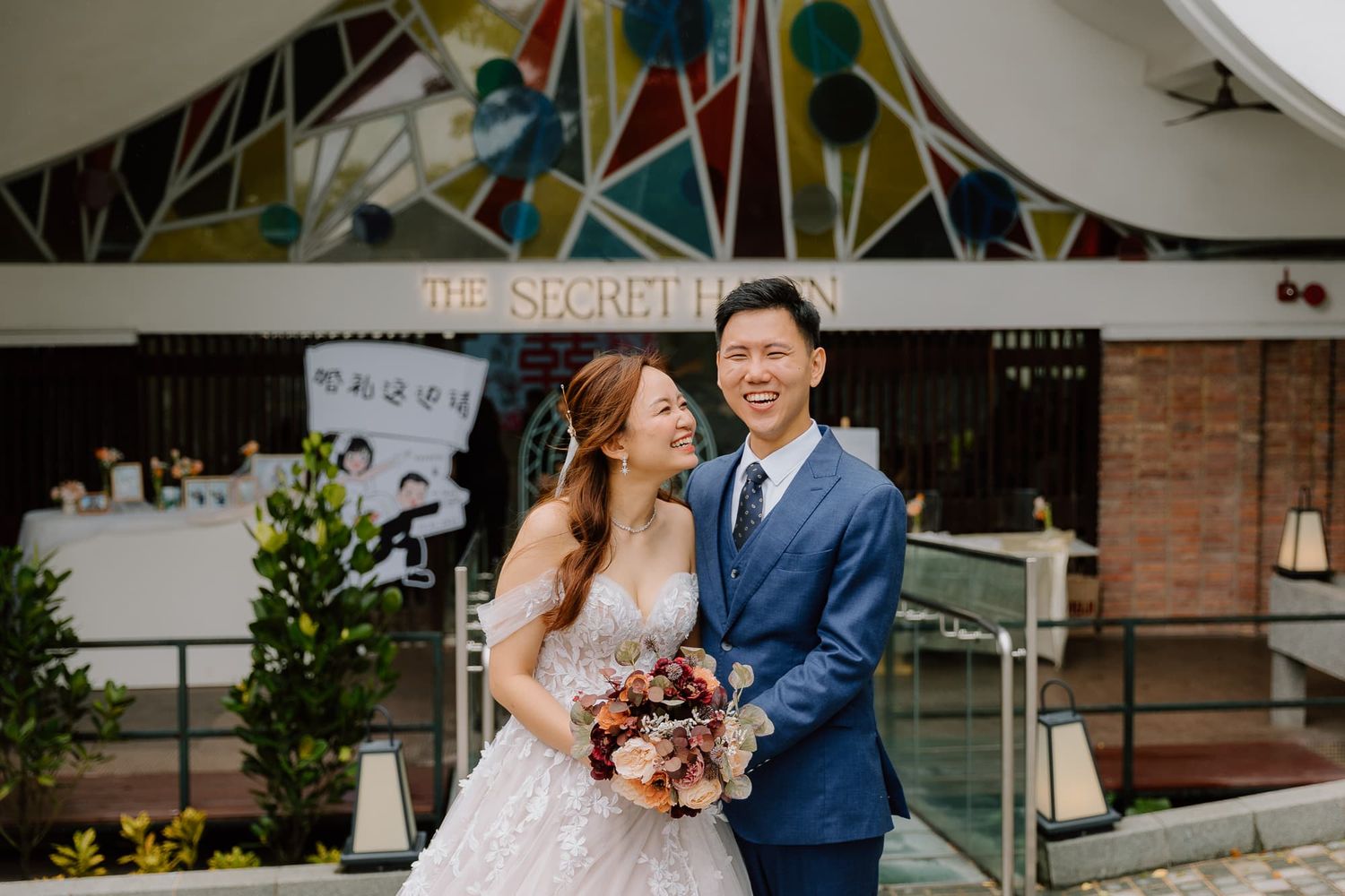 Couple sharing a laugh at wedding venue with stained glass art backdrop.