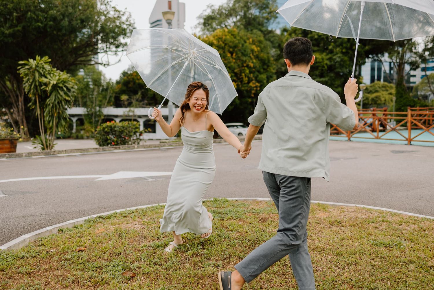 Couple dancing with transparent umbrellas in a park on a sunny day.