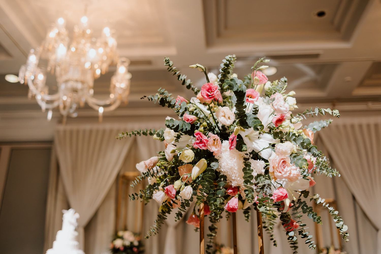Elegant wedding reception venue decorated with crystal chandeliers and pink floral arrangements.