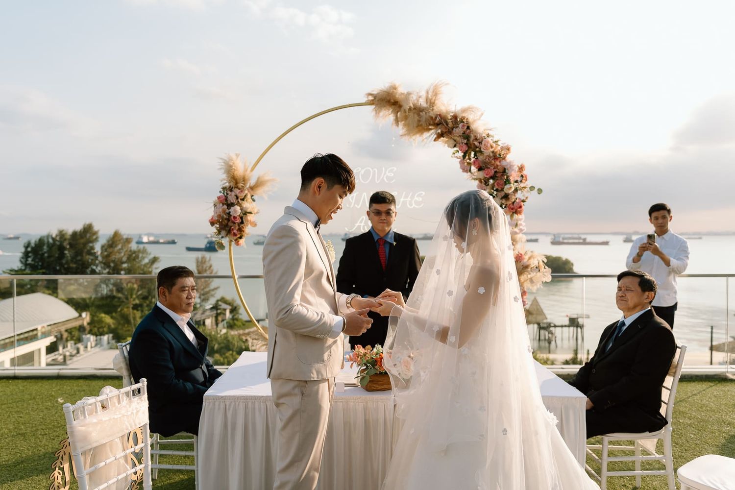 A wedding ceremony under a floral arch with ocean views in the background.
