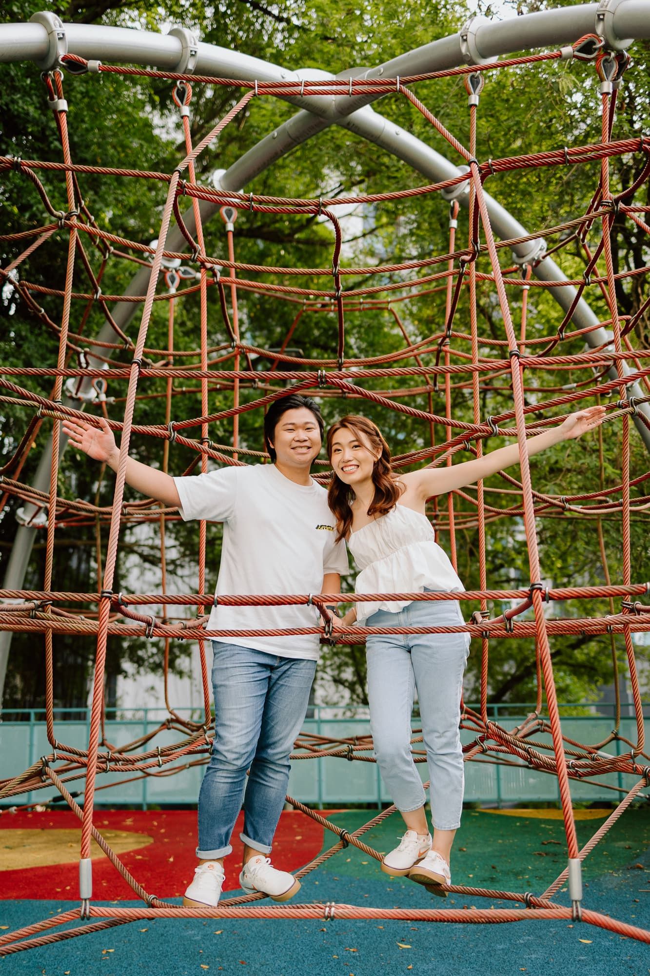 Couple posing together on red playground climbing structure in casual outfits.