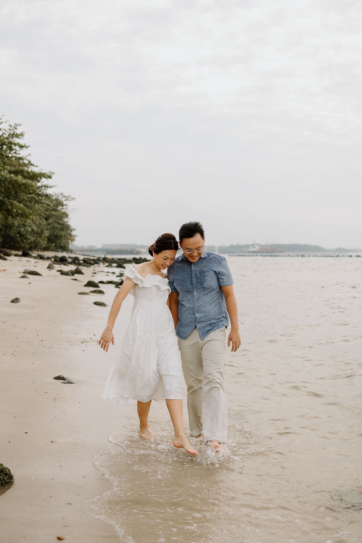 A couple walking barefoot together along a peaceful beach shoreline.