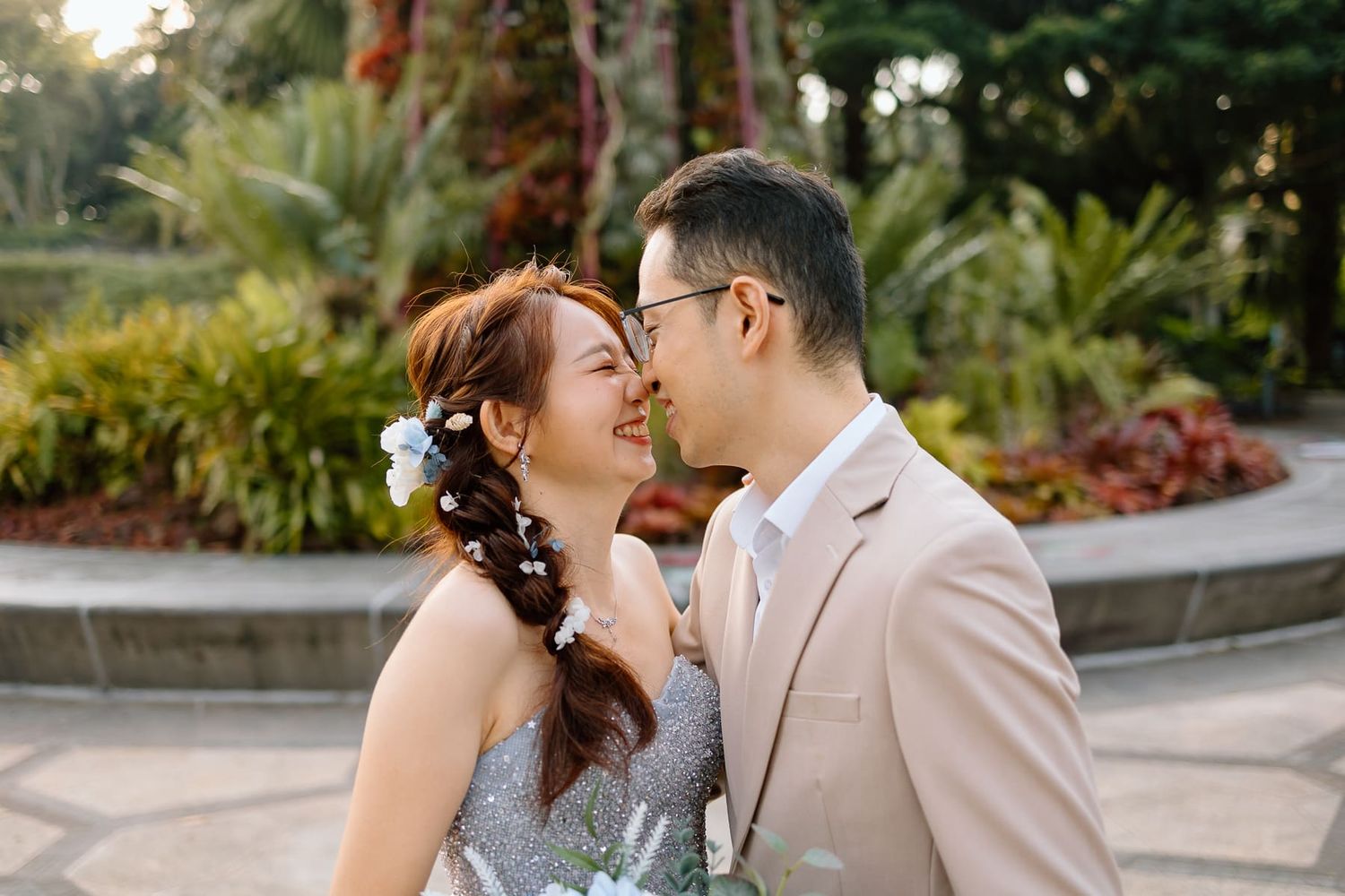 A romantic couple shares an intimate moment in formal attire against a garden backdrop.