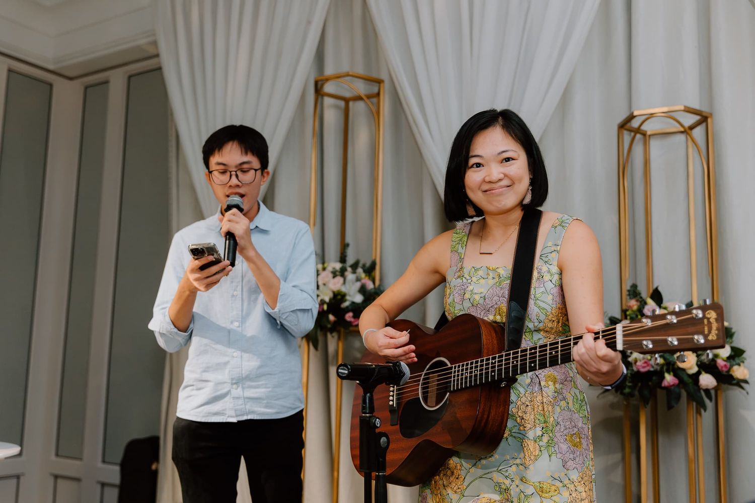 Musicians perform during wedding celebration with acoustic guitar in elegant room with white curtains.