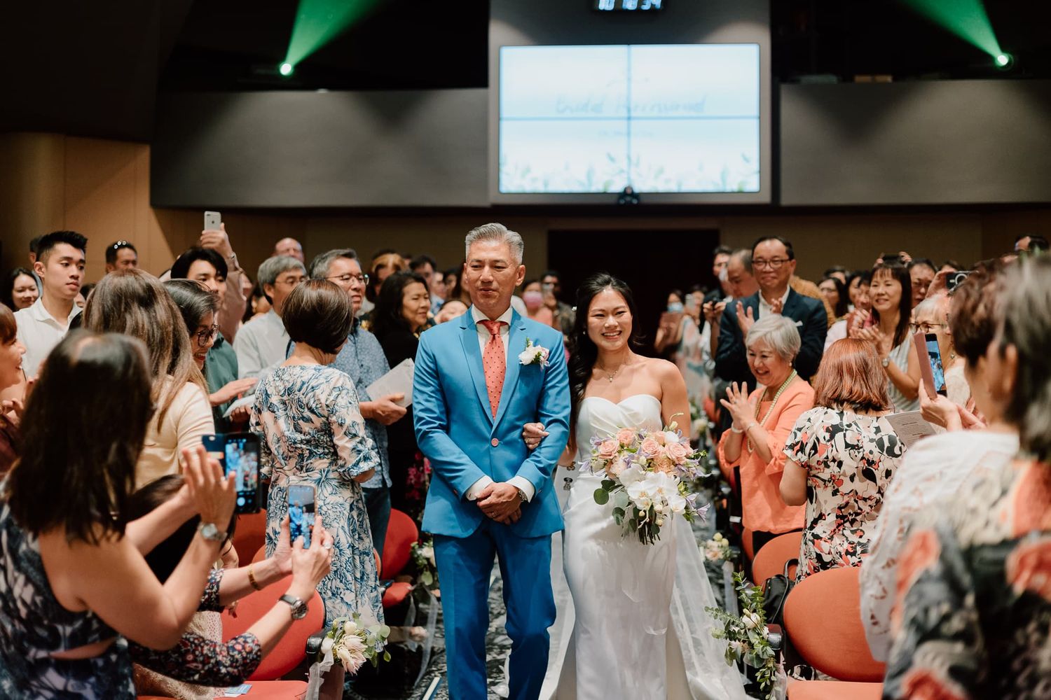 A joyous crowd of wedding guests cheers and claps during a celebration.