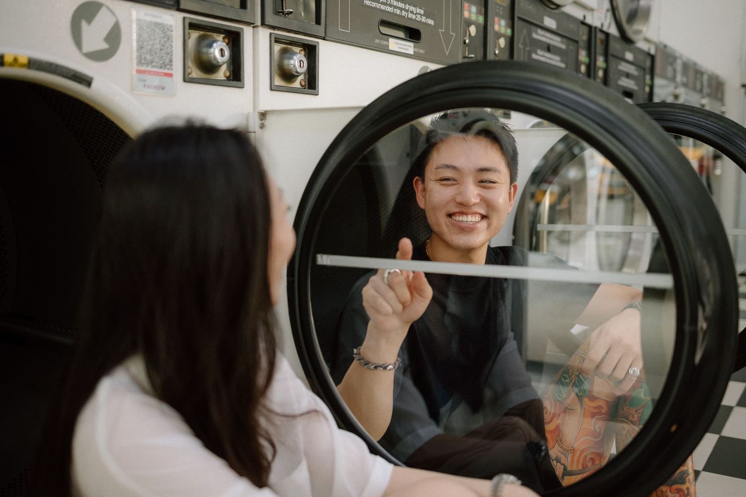 Couple shares playful moments while doing laundry at a modern laundromat with stainless steel washing machines.