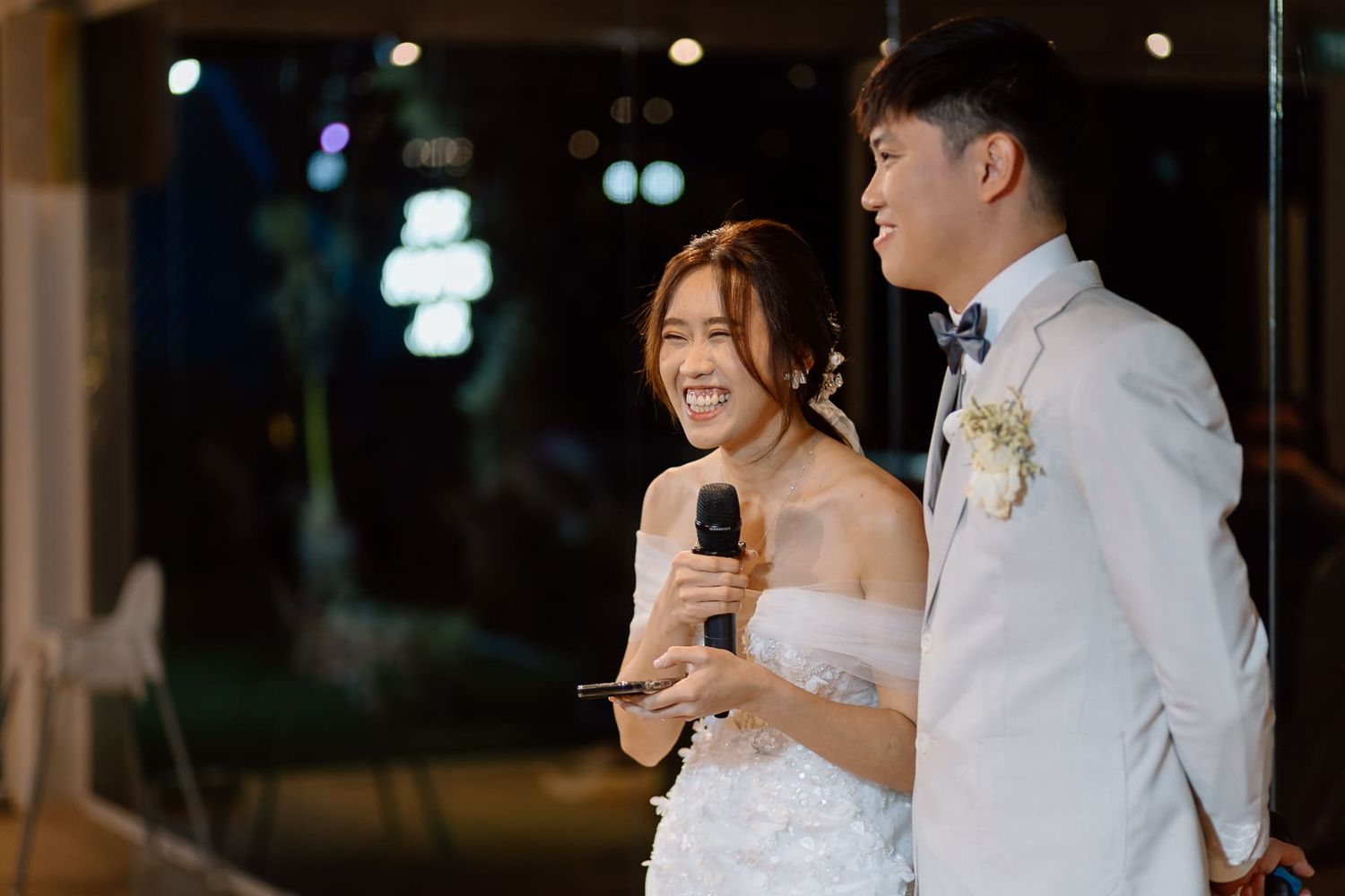 Couple sharing a joyful moment while speaking into microphones at their wedding reception.