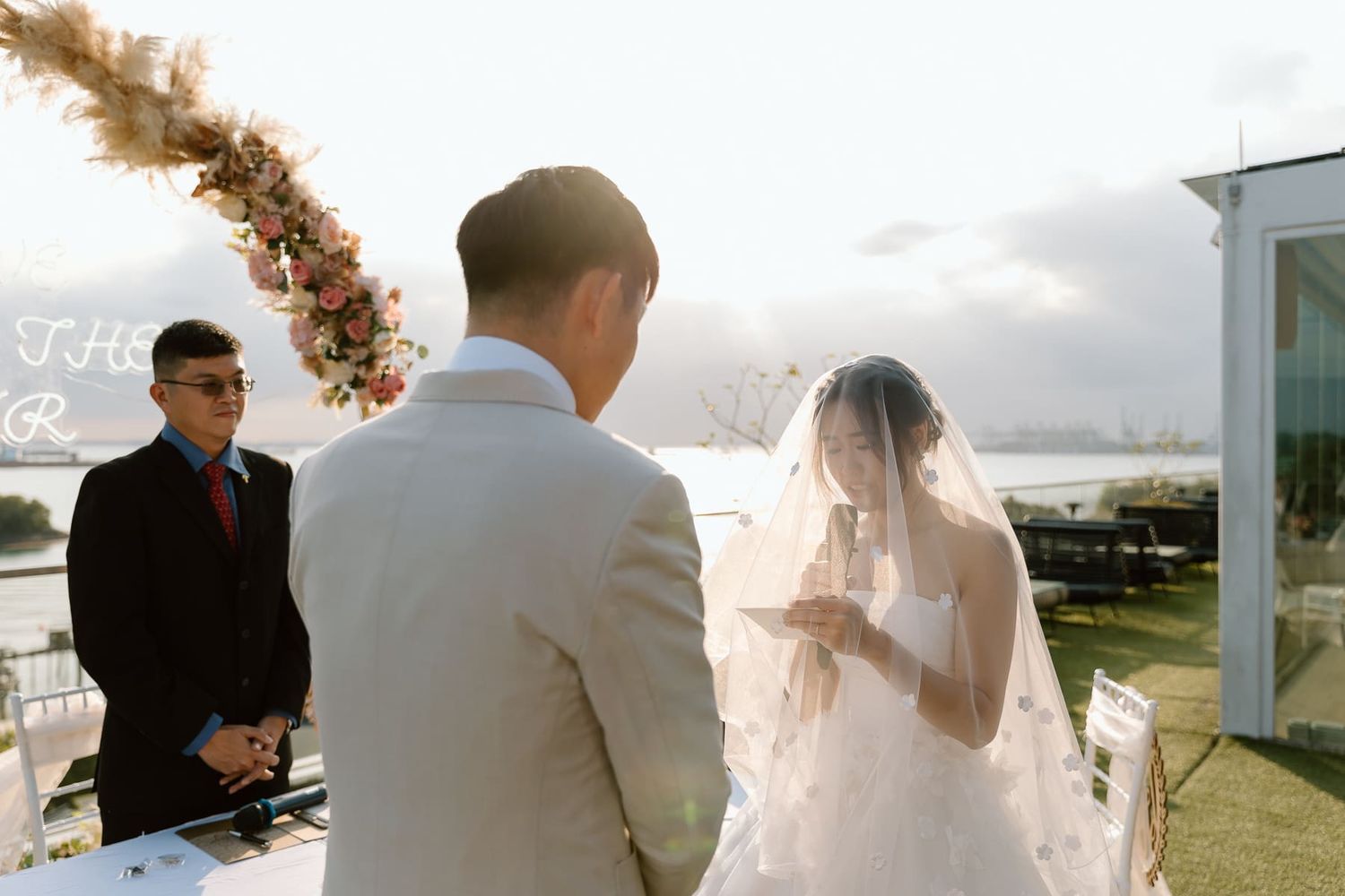 Intimate wedding ceremony moment under a decorated arch with sunset lighting.