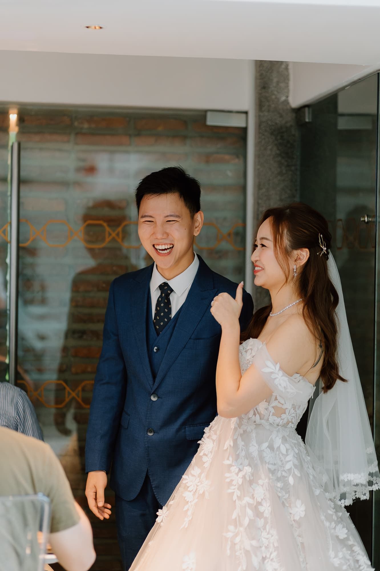 Wedding couple sharing laughter during ceremony in modern venue with brick accents.