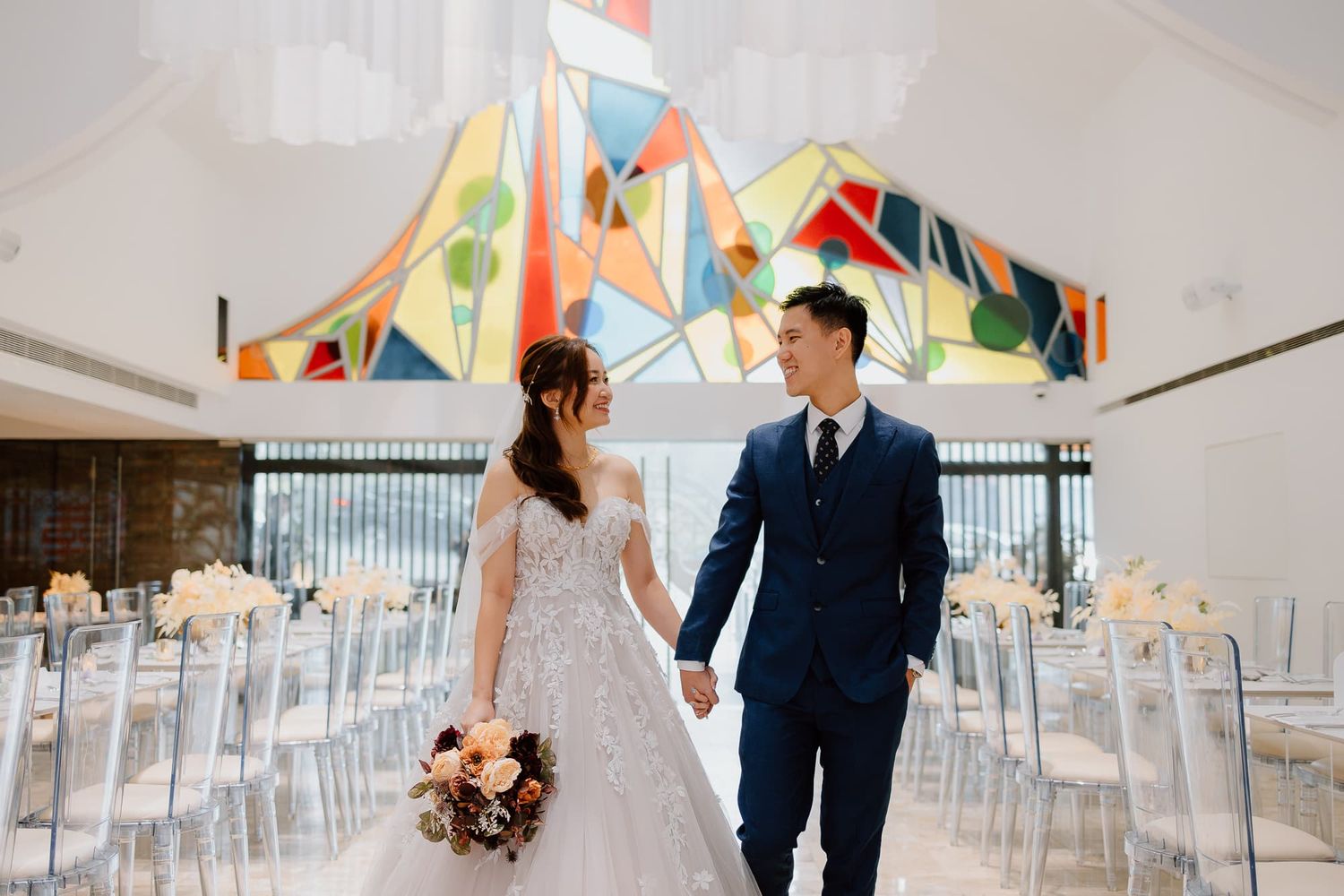 Bride and groom share intimate moments in modern wedding venue with colorful geometric backdrop.