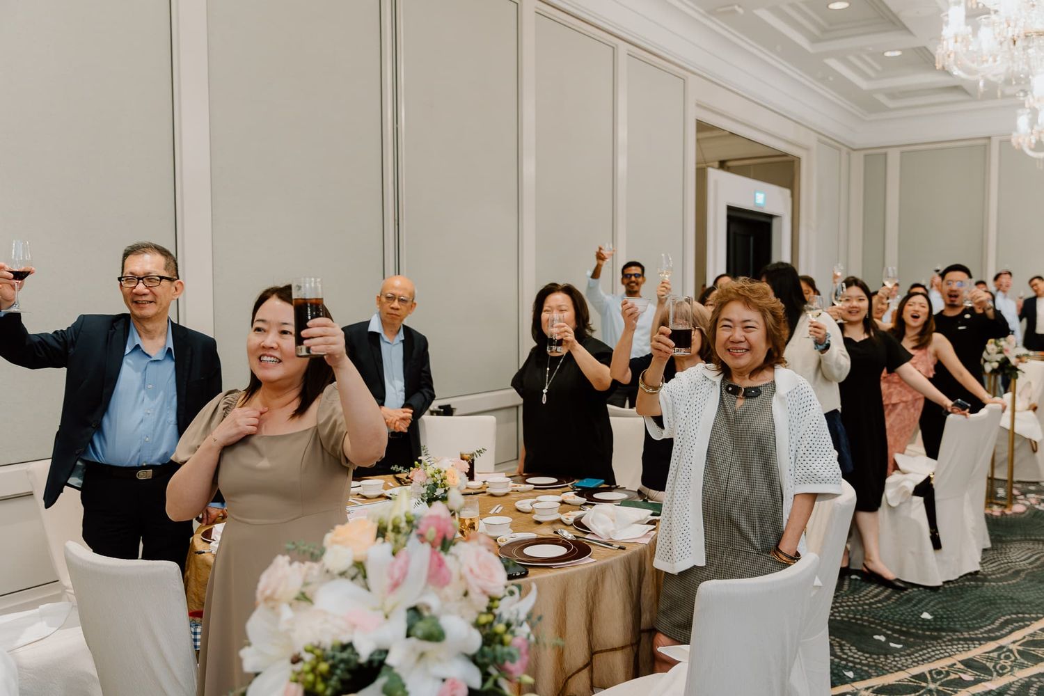 Wedding guests stand and cheer during a festive reception celebration.