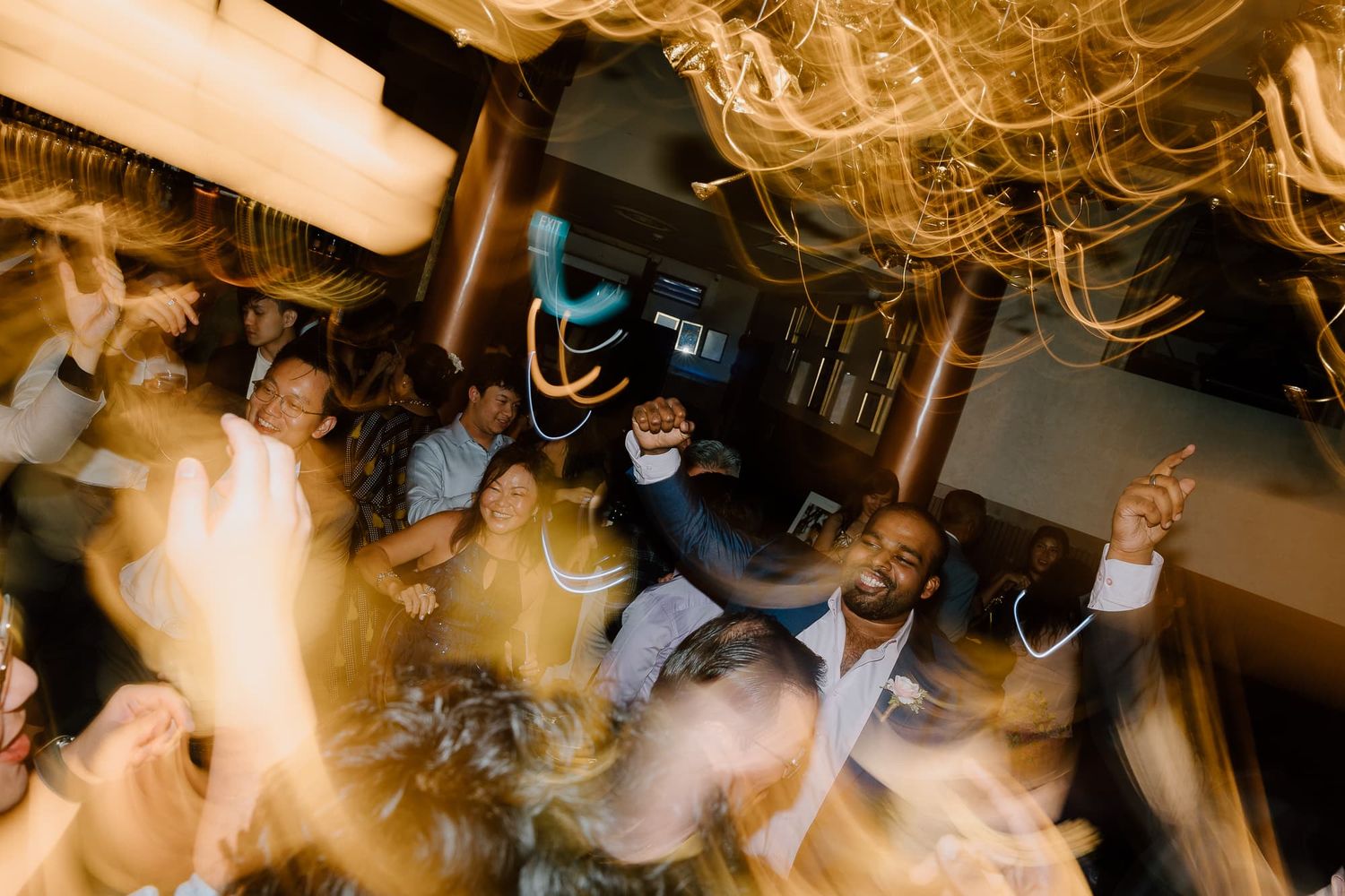 Motion-blurred photo of party guests dancing energetically in a dark venue with dramatic lighting.