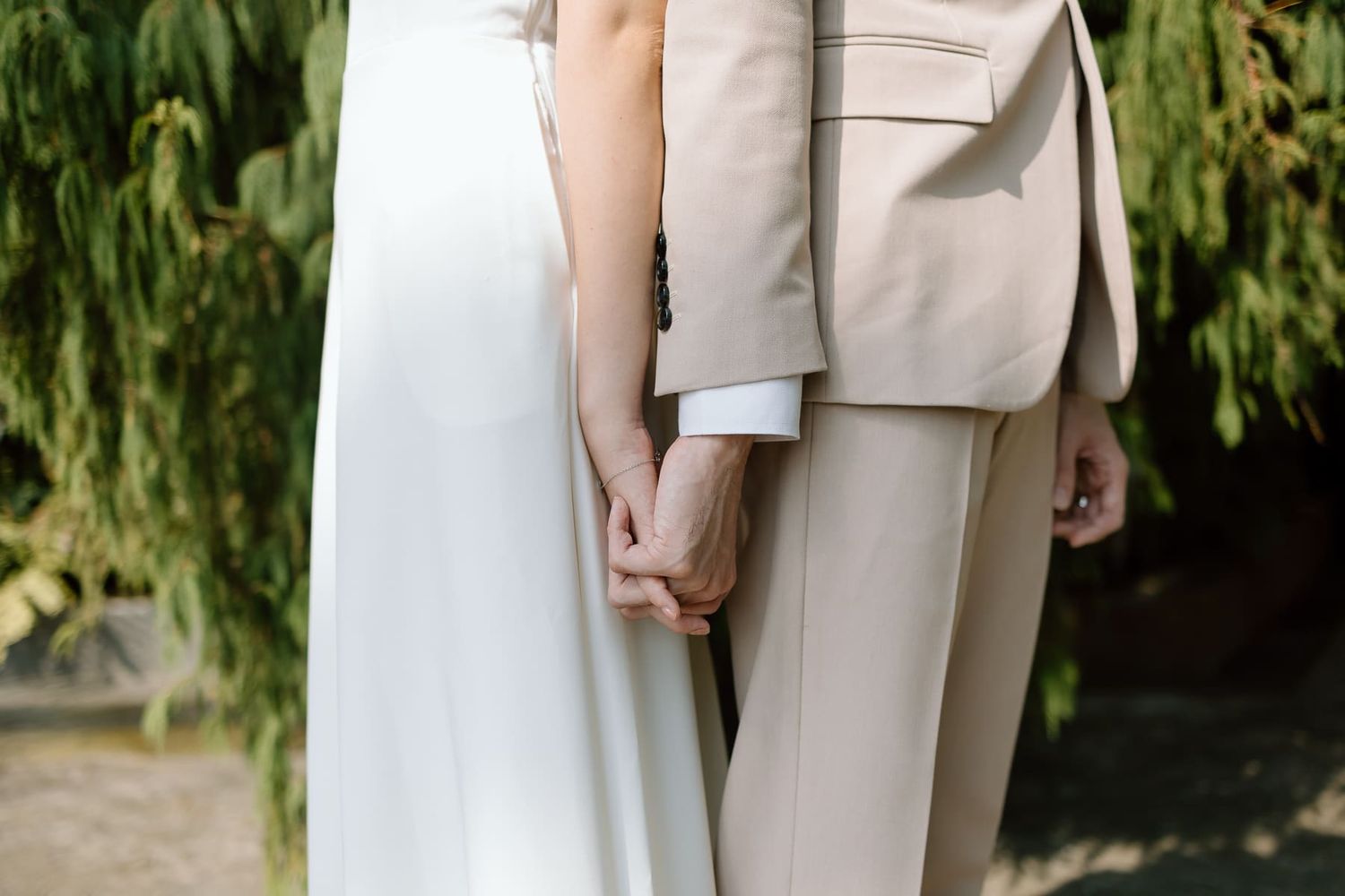 A close-up shot of a couple holding hands, with one in white dress and another in beige suit.