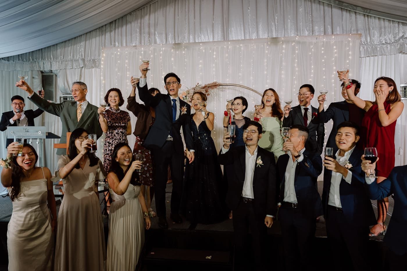 Large group of wedding guests and attendants celebrating with raised arms.