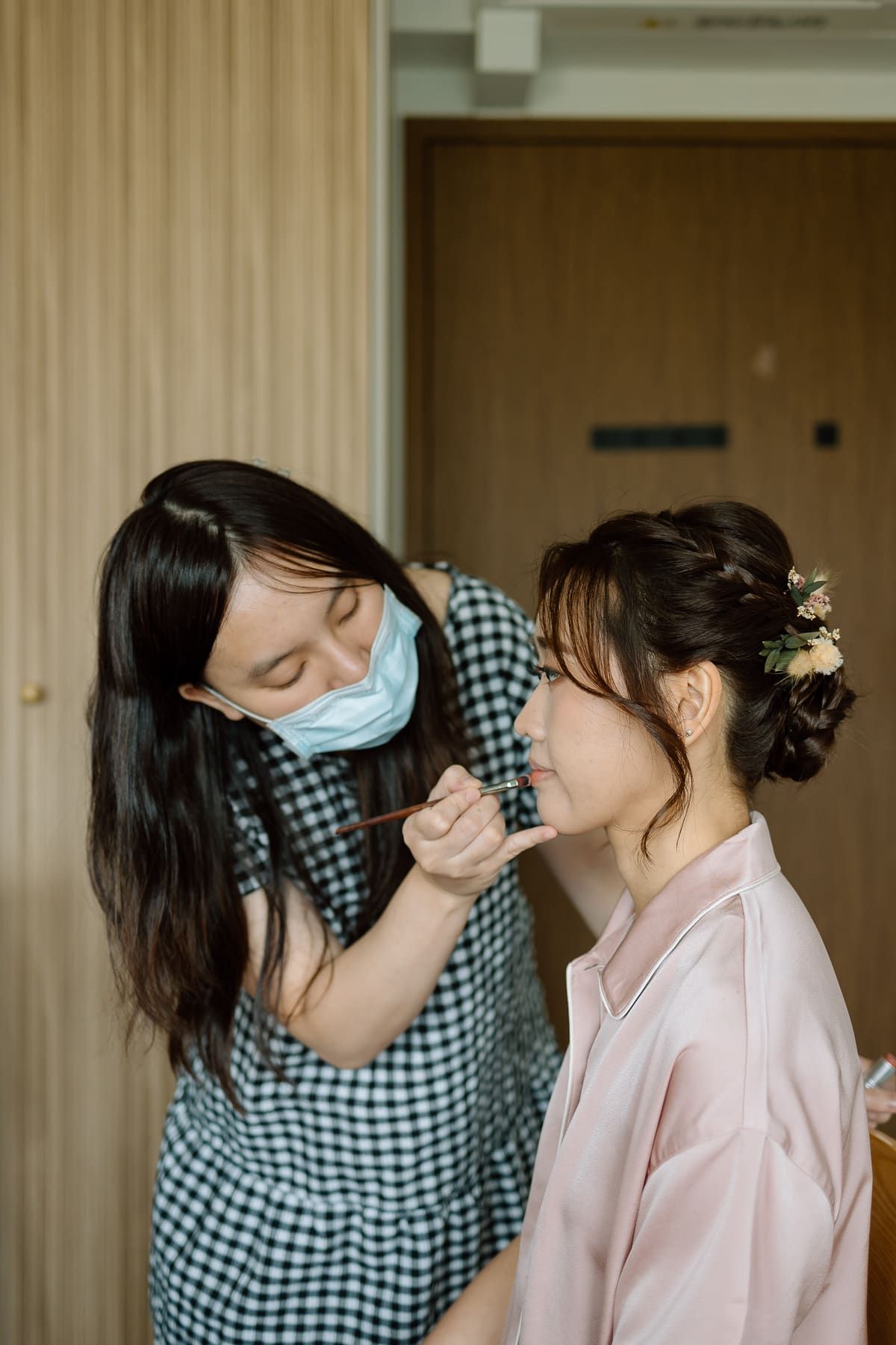 A makeup artist applying cosmetics to someone in a pink robe during wedding preparations.