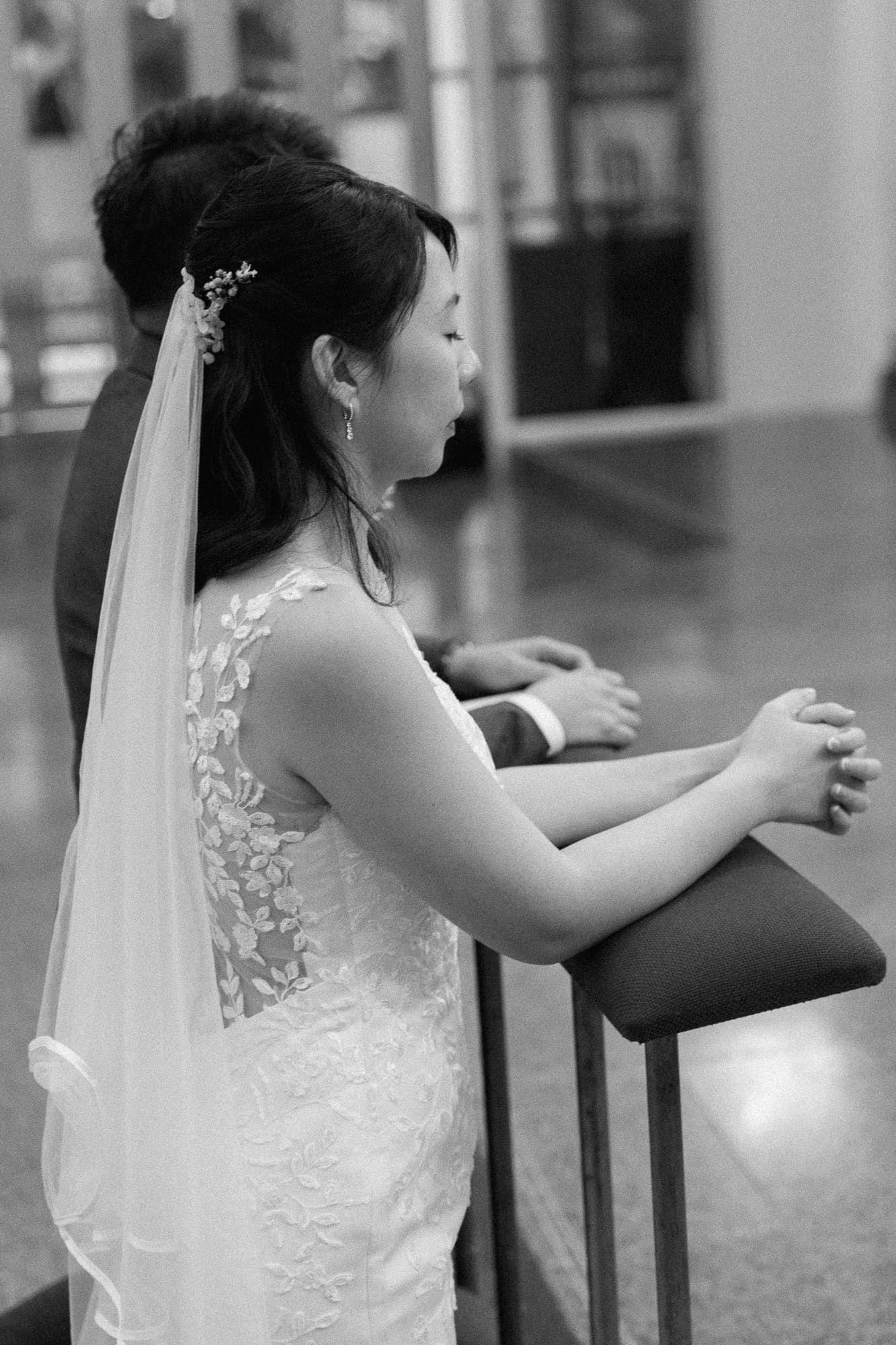 A bride in a white lace wedding dress with an illusion back and cathedral veil stands elegantly in black and white.