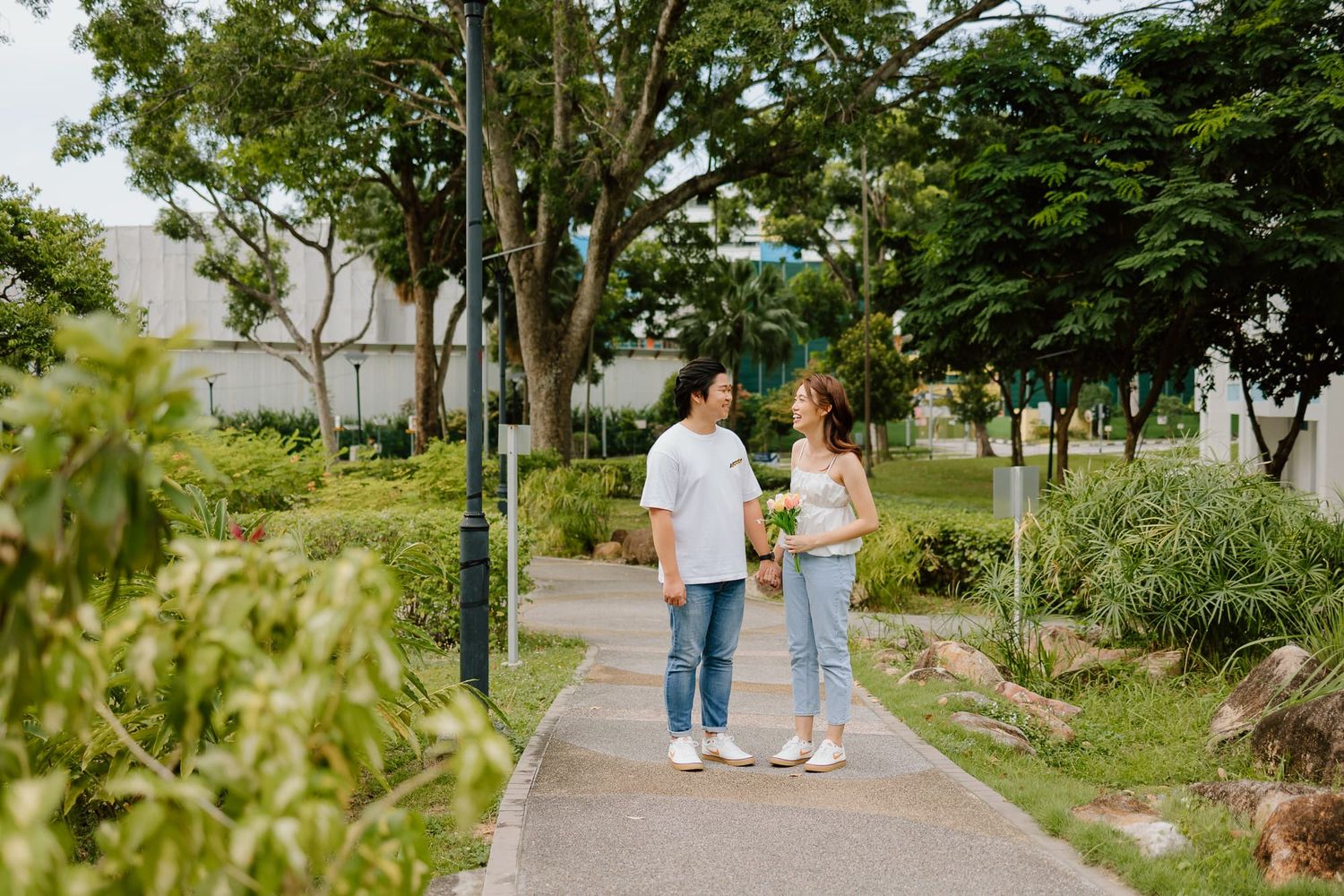 Casual couple strolling along tree-lined pathway in park.