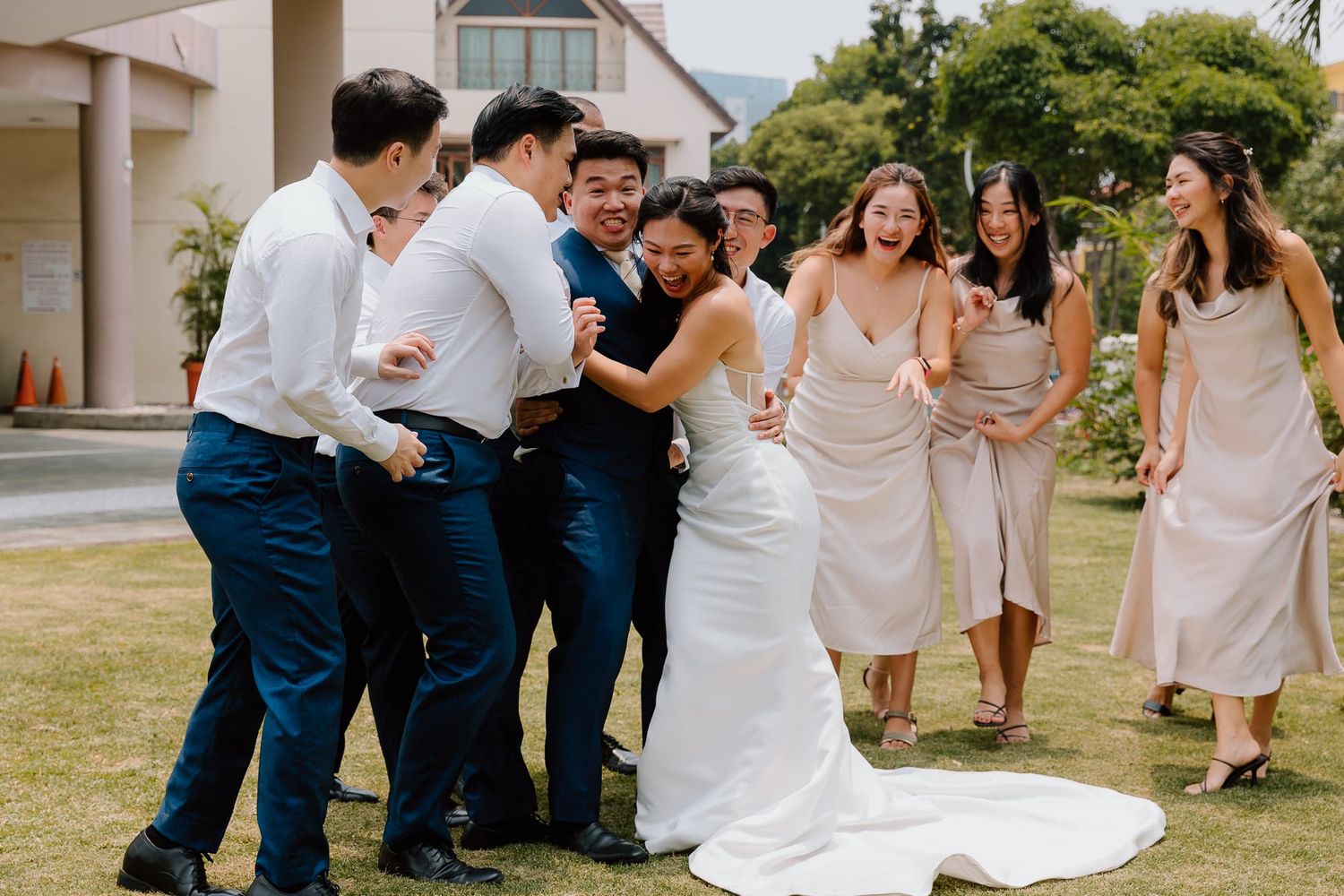 Wedding party members in navy suits and blush dresses laugh together during outdoor celebration.