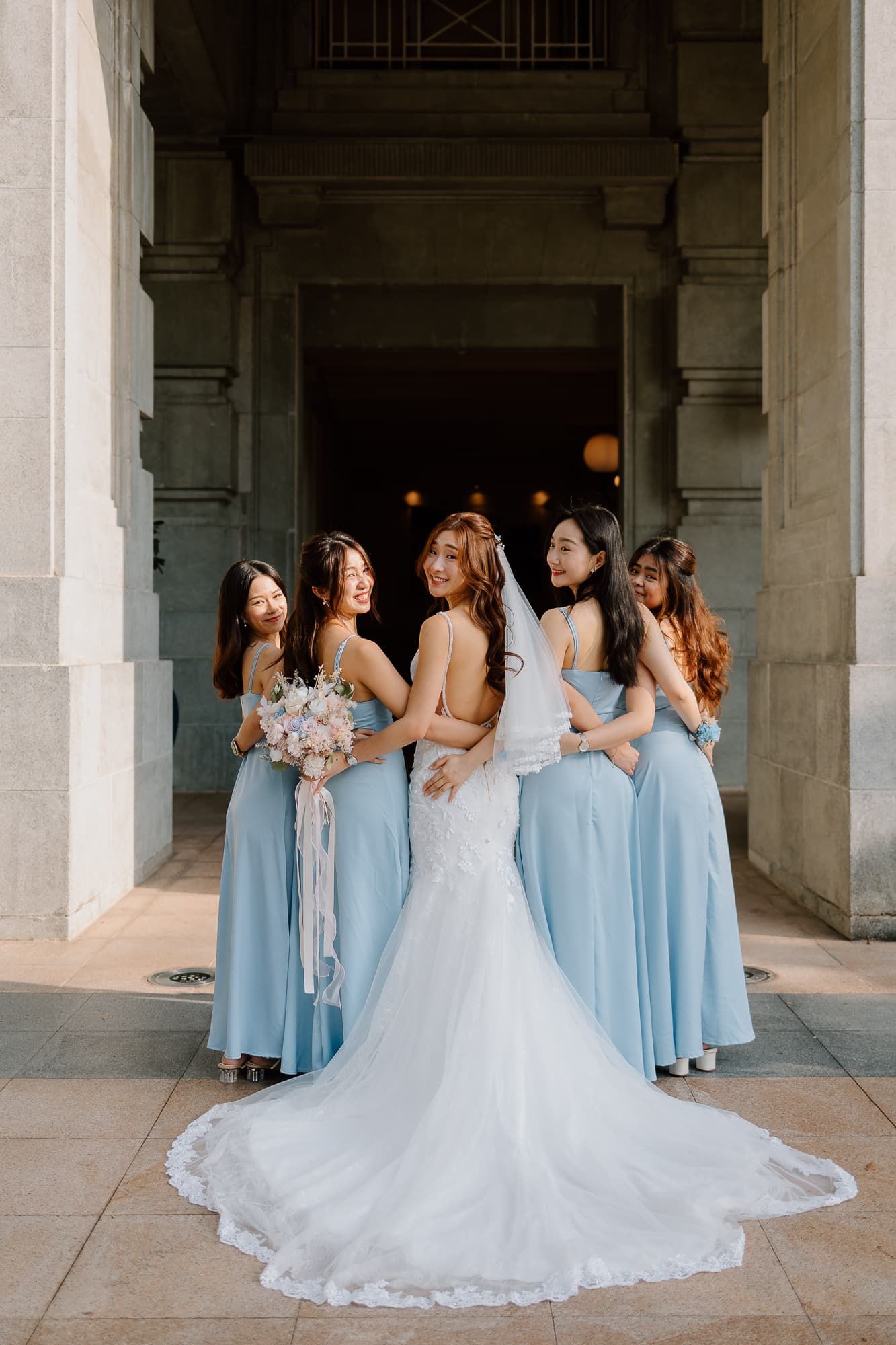 Wedding party in light blue bridesmaid dresses gathered around a flowing white wedding gown.