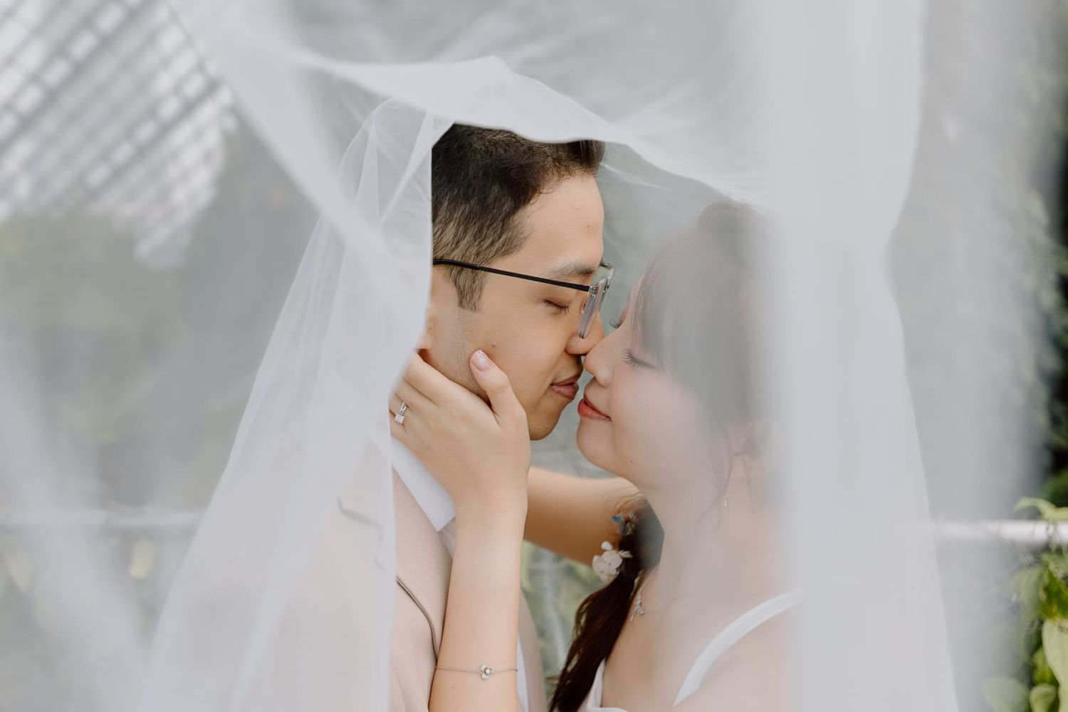 An intimate moment shared under a flowing veil in soft natural light.