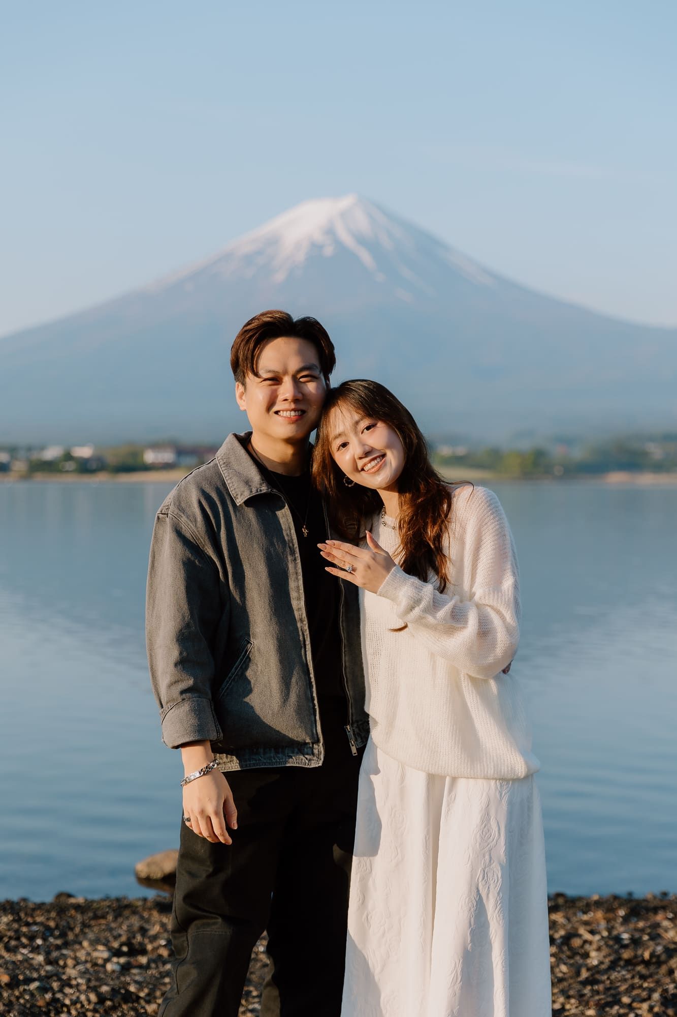 A smiling couple poses together in front of Mount Fuji and a serene lake in Japan.