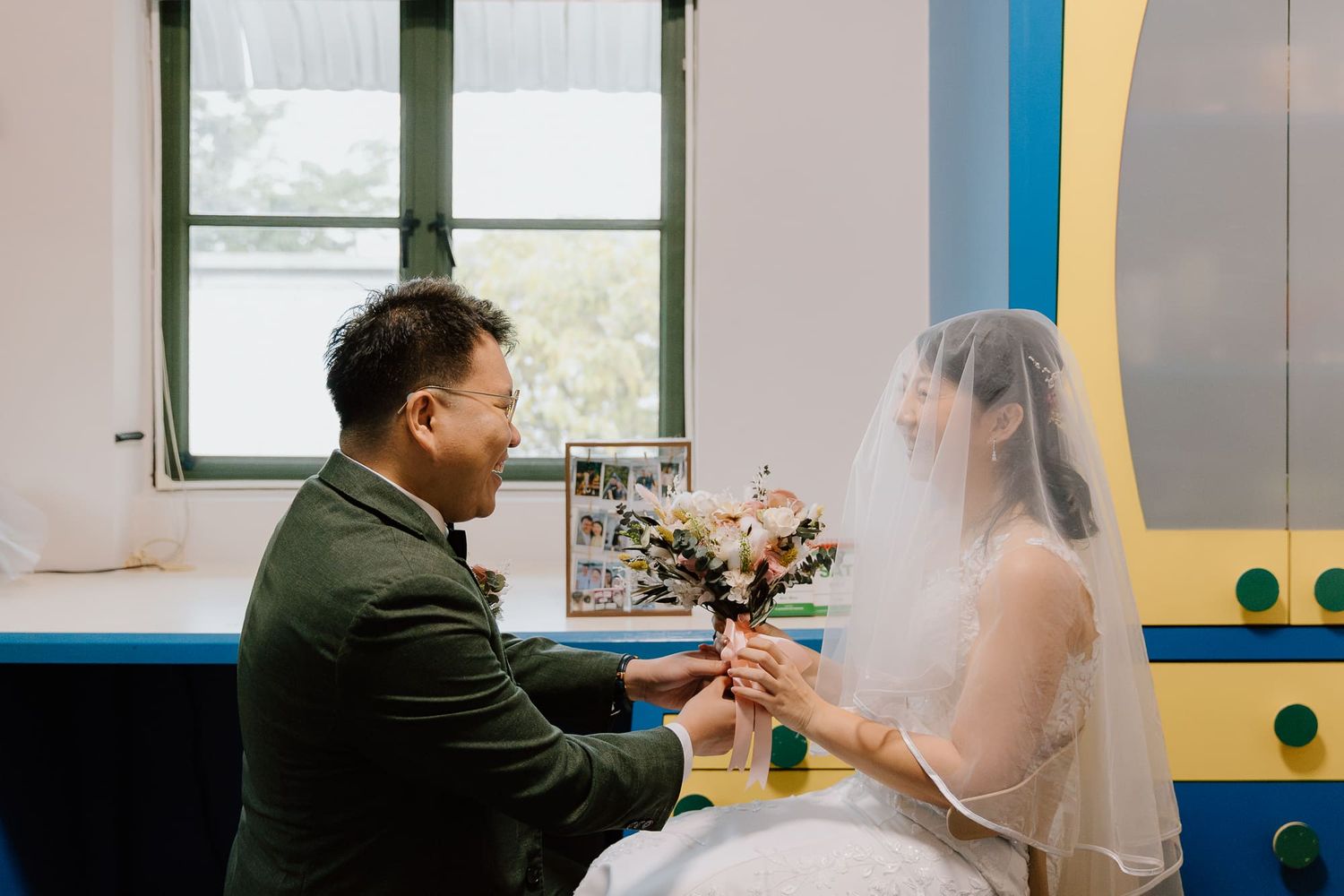 A bride and groom share an intimate moment in a naturally lit room with colorful floral decorations.