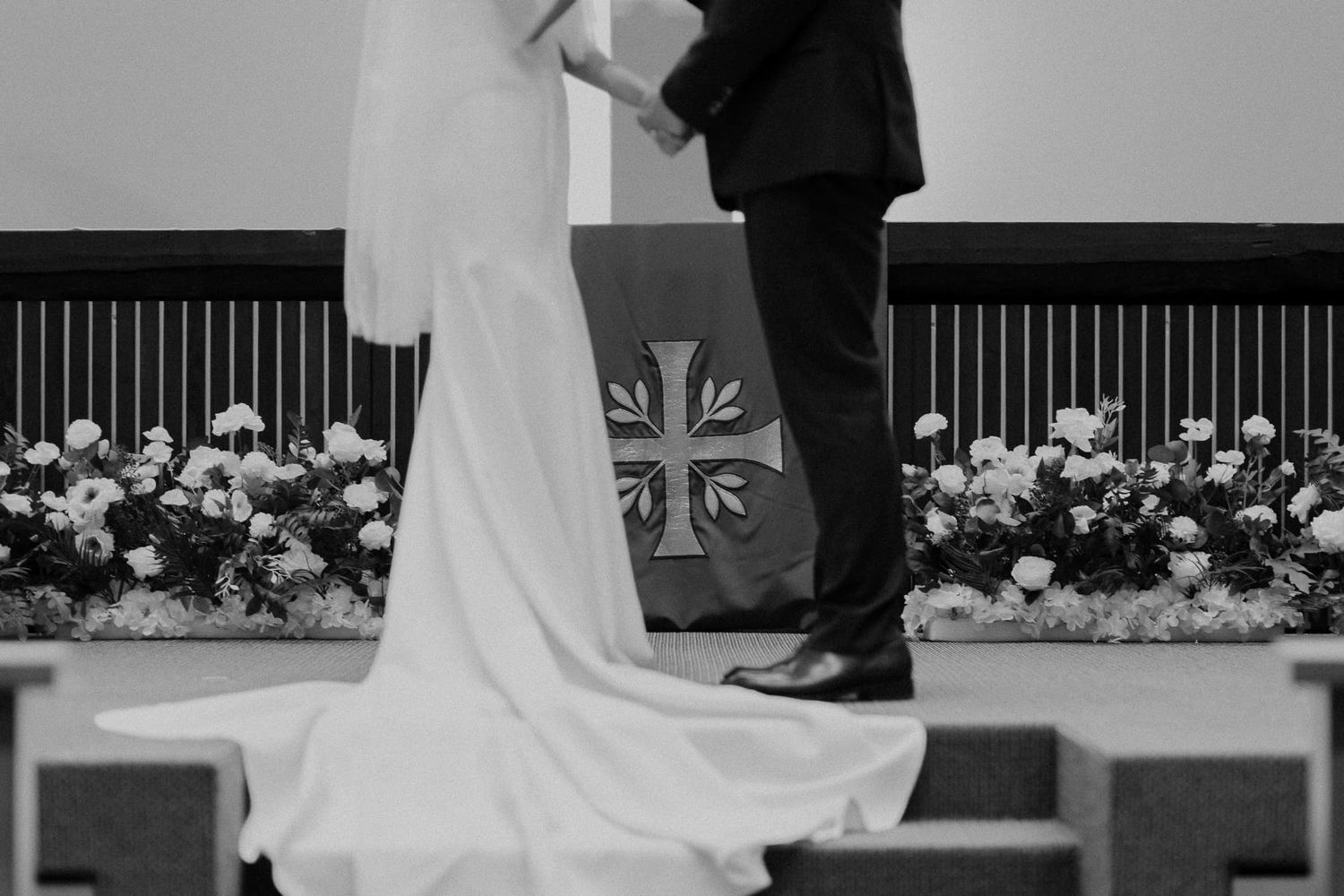 Elegant church wedding ceremony with white floral arrangements and cross backdrop.