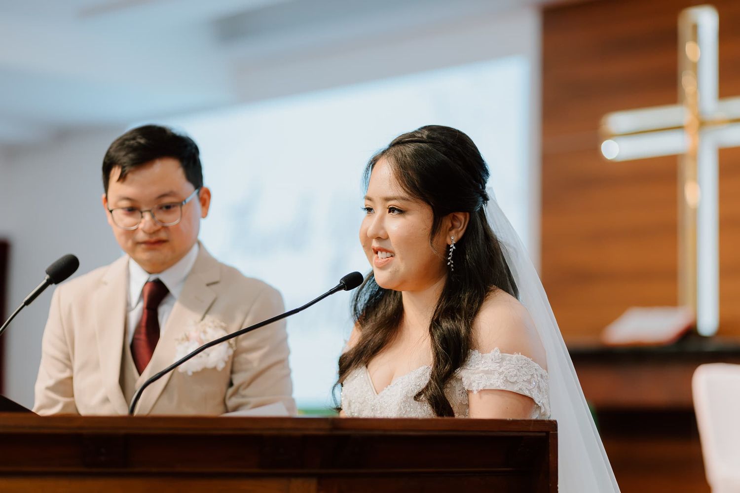 Couple speaks at church podium during wedding ceremony with wooden cross backdrop.