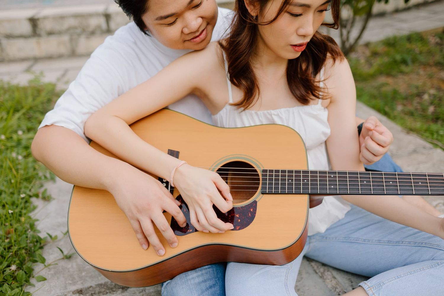 Two people sharing intimate moment while playing acoustic guitar outdoors.