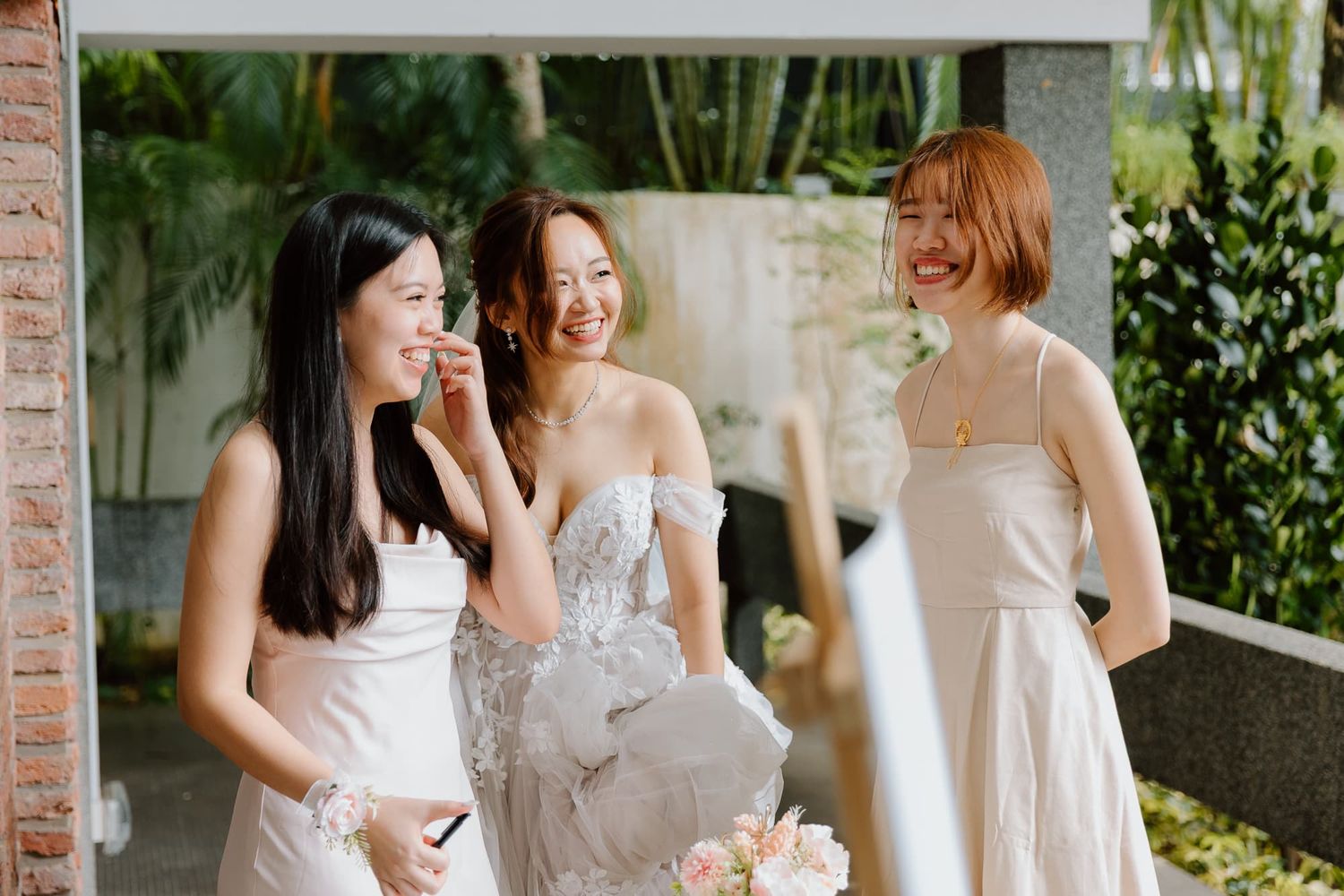 Three guests in light-colored dresses sharing a joyful moment at an outdoor wedding venue.