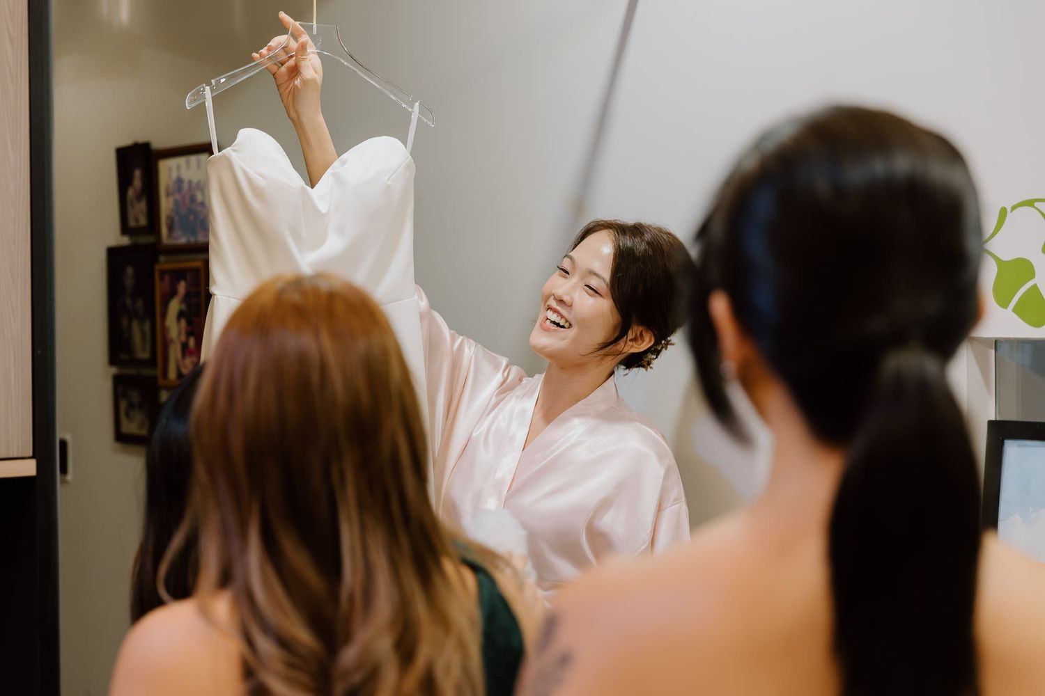 A pleasant moment during wedding preparations with a white wedding dress being held up in a room.