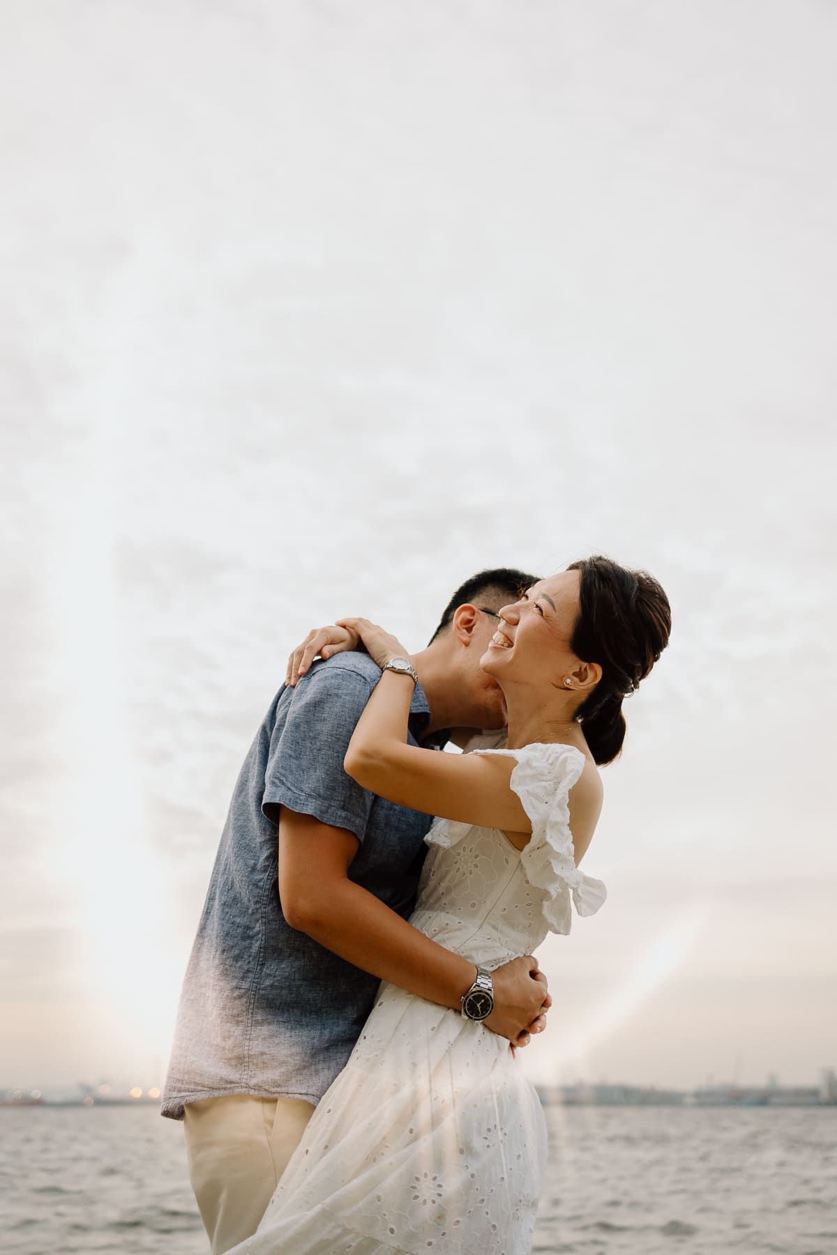 A romantic embrace captured against a cloudy sky and ocean backdrop.