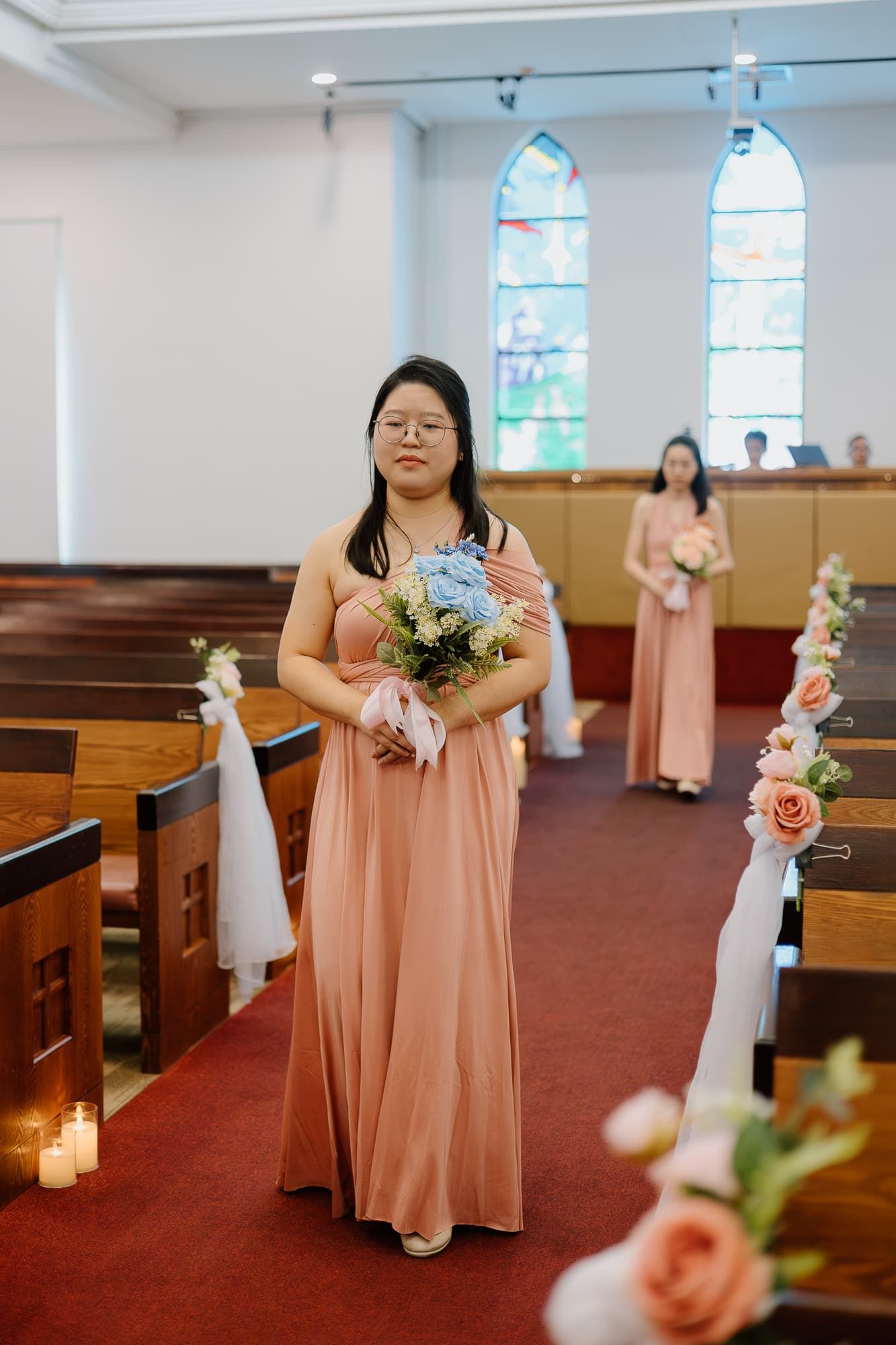 Wedding ceremony in a church with stained glass windows and floral pew decorations.