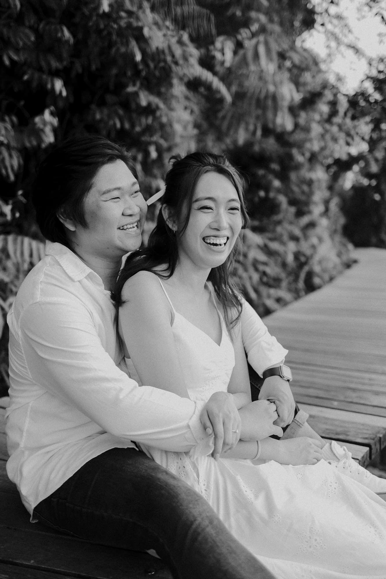 Black and white portrait of couple laughing together on wooden bench.