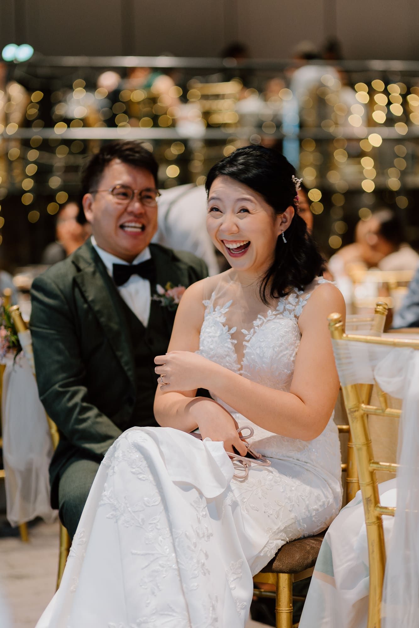 Wedding guests at an elegant reception share laughter and joy around tables decorated with golden chairs and twinkling lights.