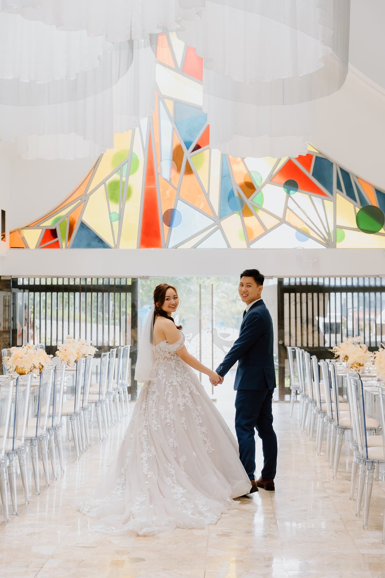 Wedding couple poses in elegant venue featuring geometric art and clear ghost chairs.