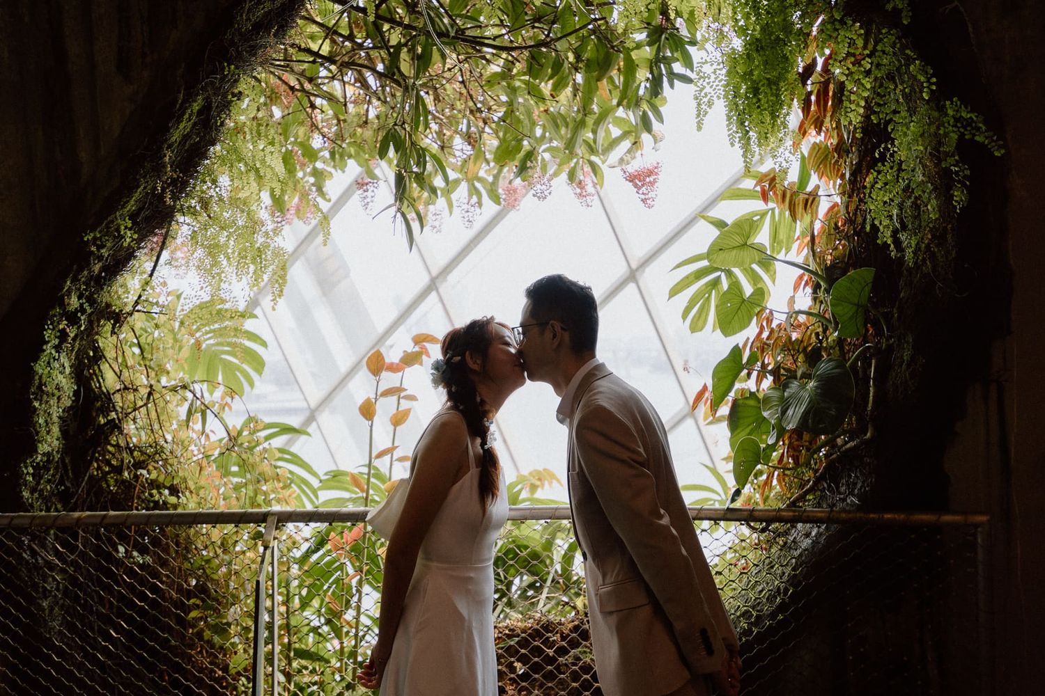 A romantic silhouette of a couple sharing an intimate moment under a lush green archway.