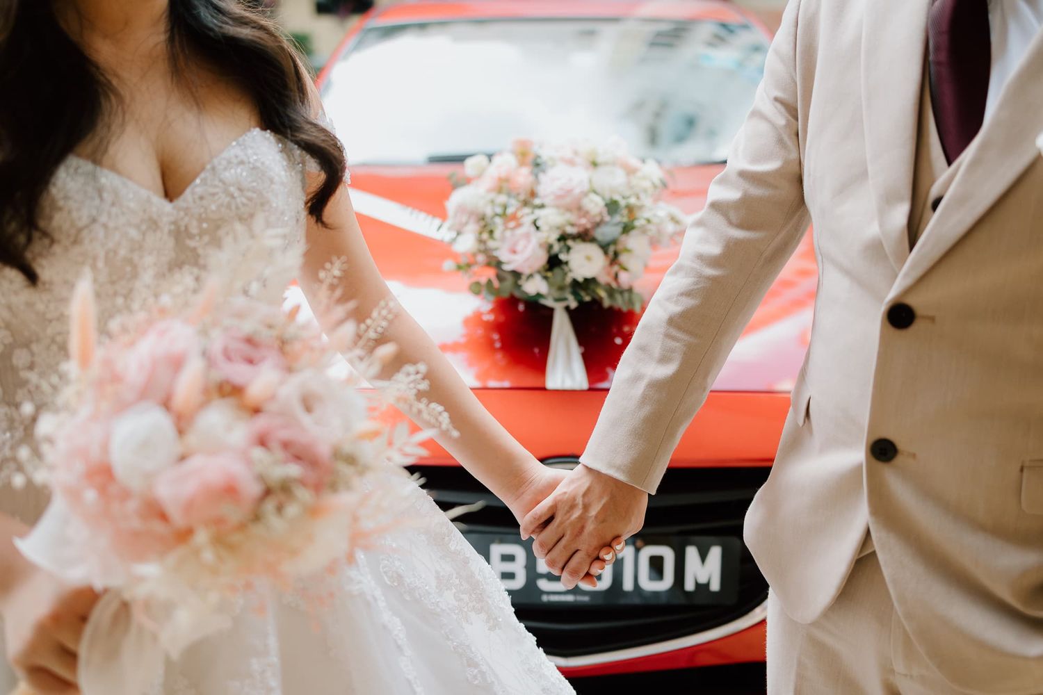 Pink floral wedding bouquets rest against a red vehicle.