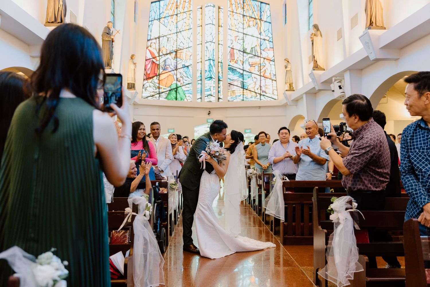 Joyful moment in a church aisle during an intimate wedding ceremony with guests seated on wooden pews.