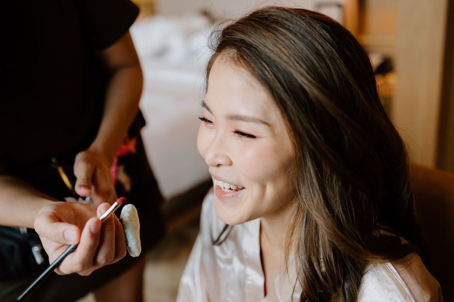 A person getting their makeup done while smiling during a bridal preparation session.