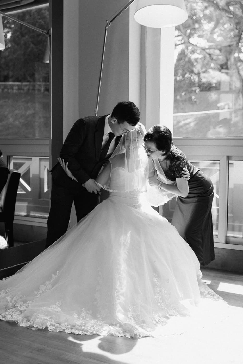 Black and white image of wedding dress being adjusted in a sunlit room.