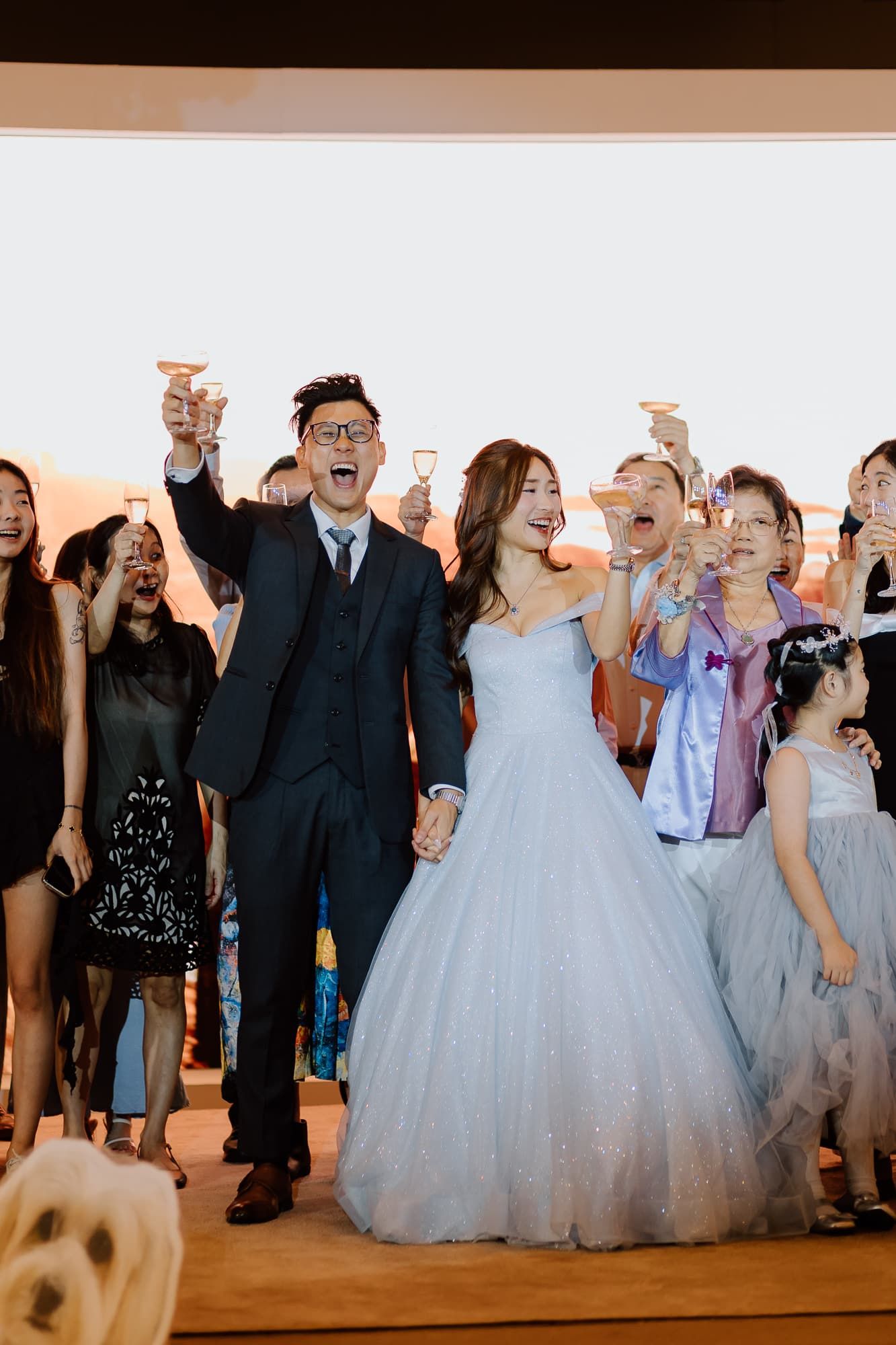 Joyful wedding celebration with guests raising glasses in a toast on the dance floor.